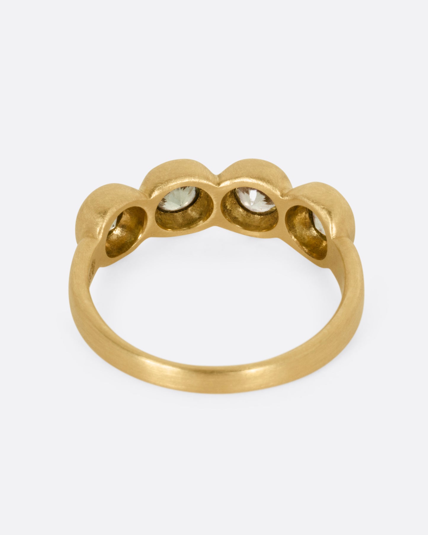 A yellow gold ring with four bezel set green sapphires, shown from the back.