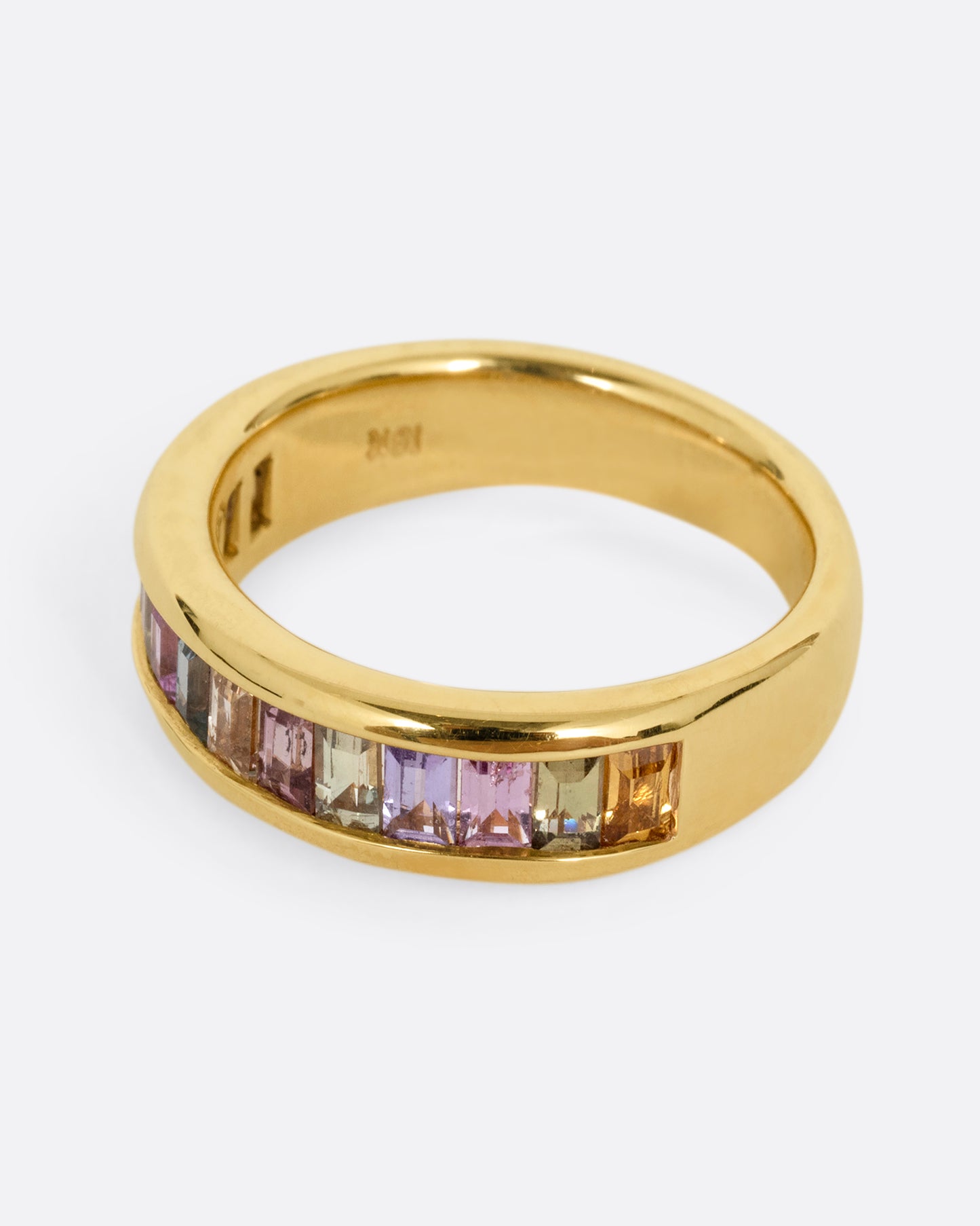 A yellow gold ring with channel set multicolored sapphires. Shown from the side.