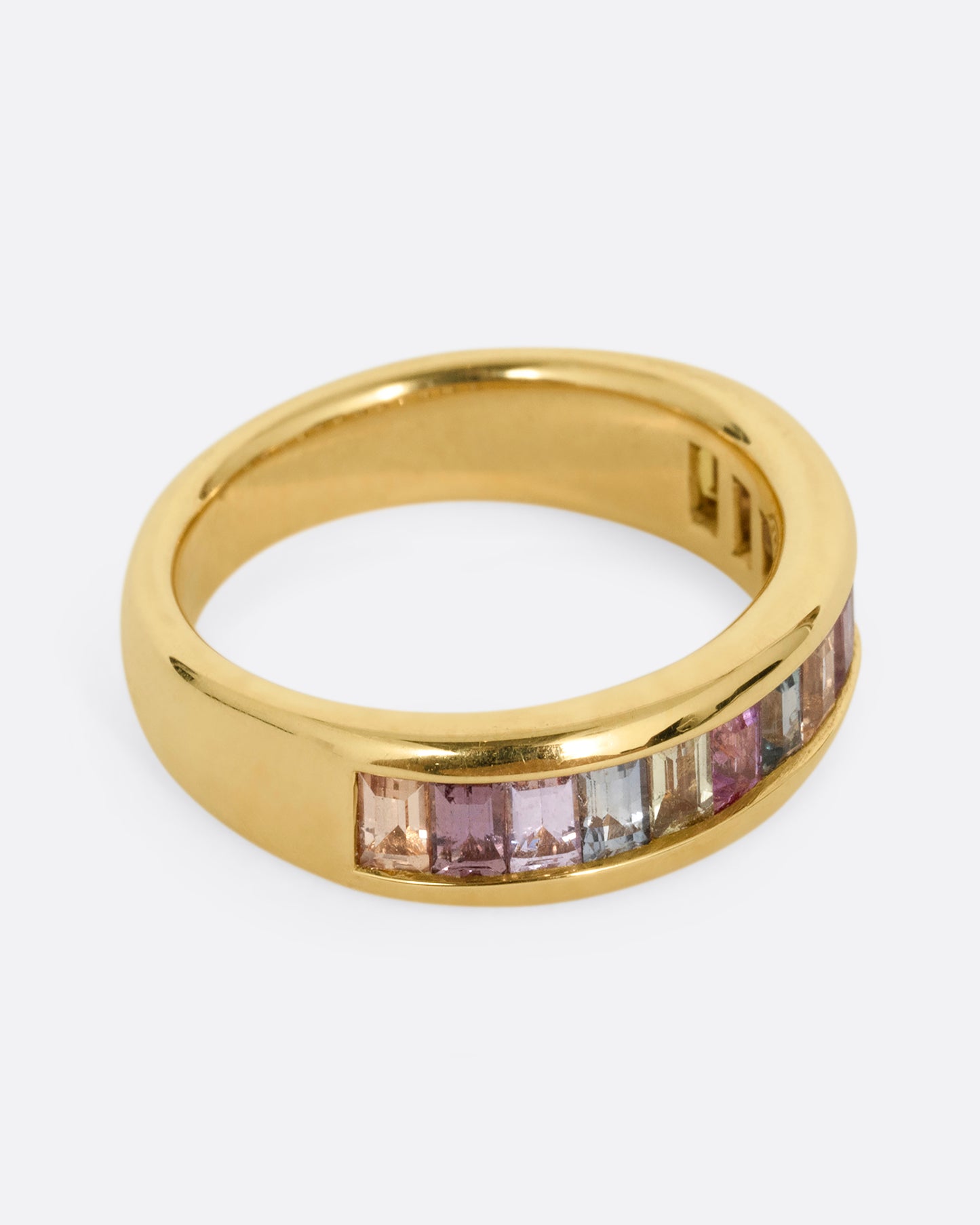 A yellow gold ring with channel set multicolored sapphires. Shown from the side.