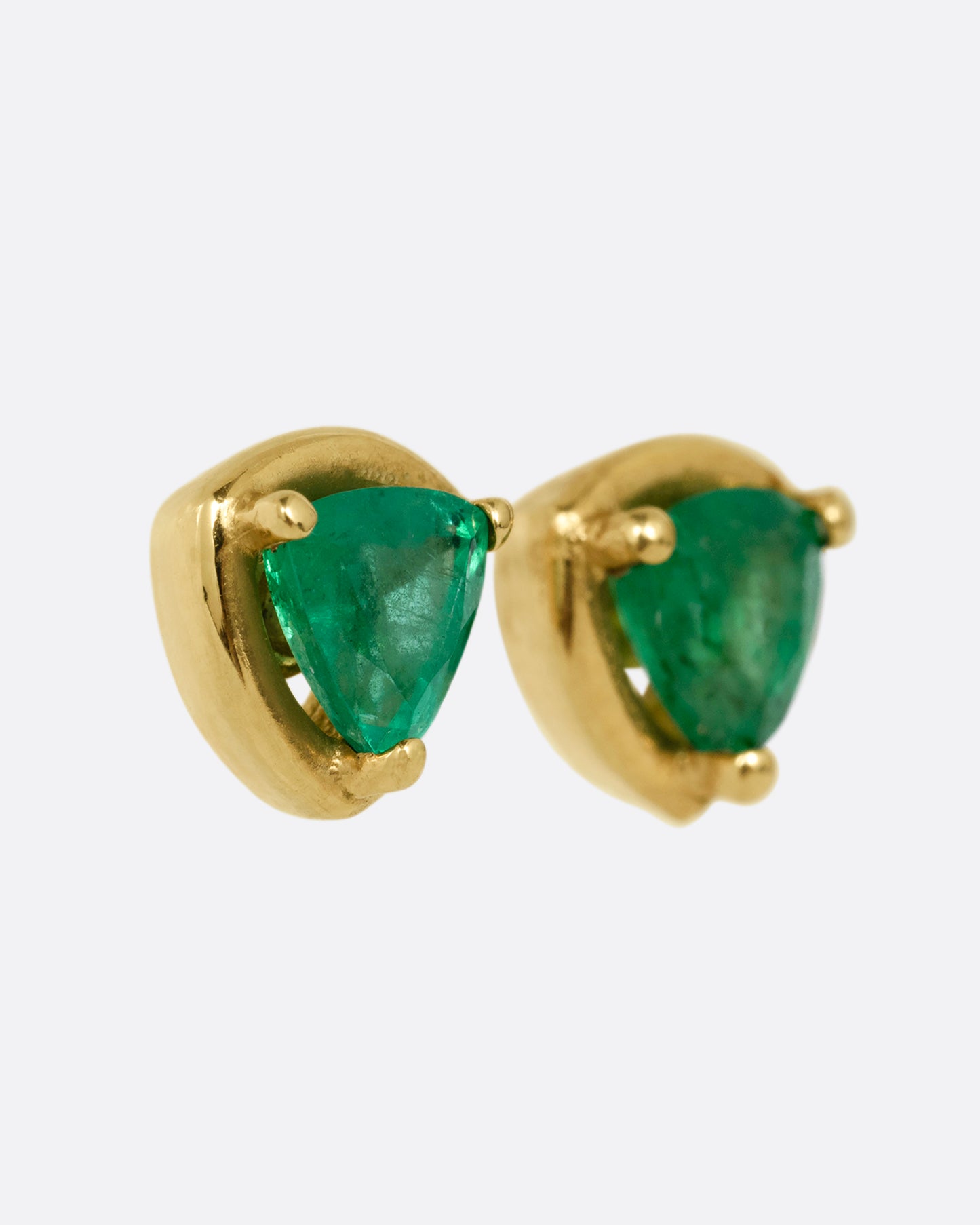 A pair of yellow gold stud earrings with emeralds. Shown from the side.