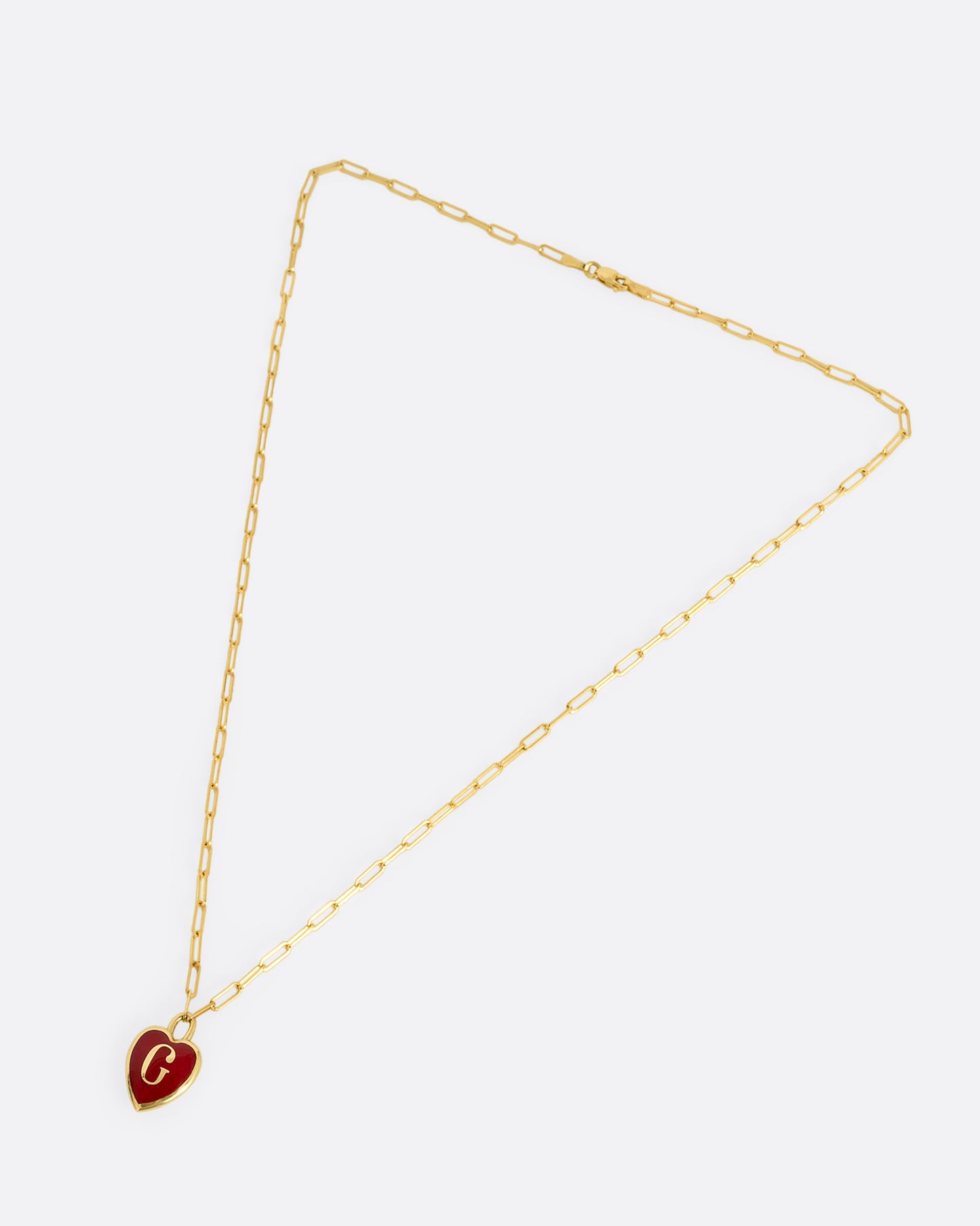 A yellow gold paperclip chain necklace with a red enamel heart shaped G pendant. Shown closed lying flat at an angle from the front.