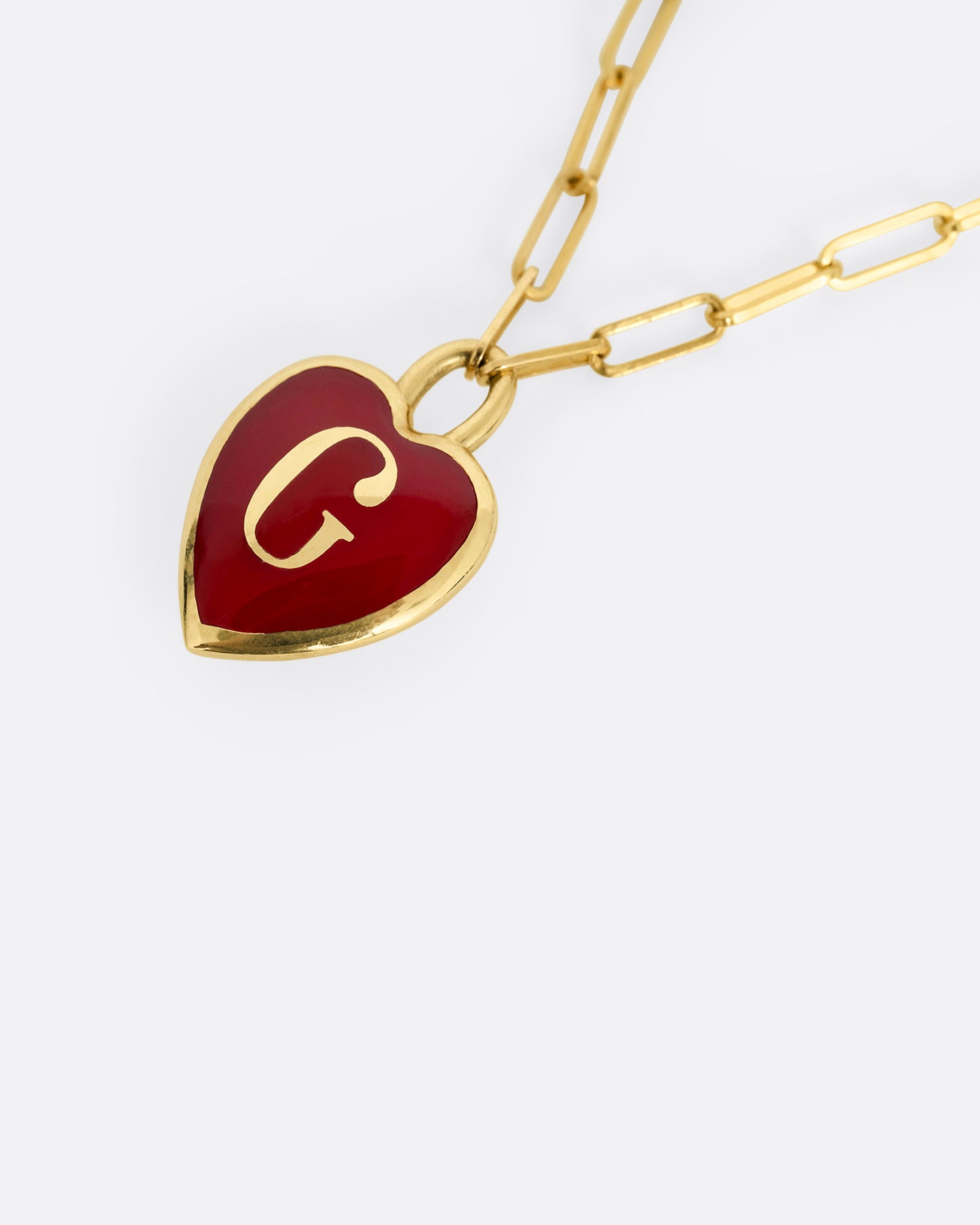 A yellow gold paperclip chain necklace with a red enamel heart shaped G pendant. Shown lying flat at an angle from the front.