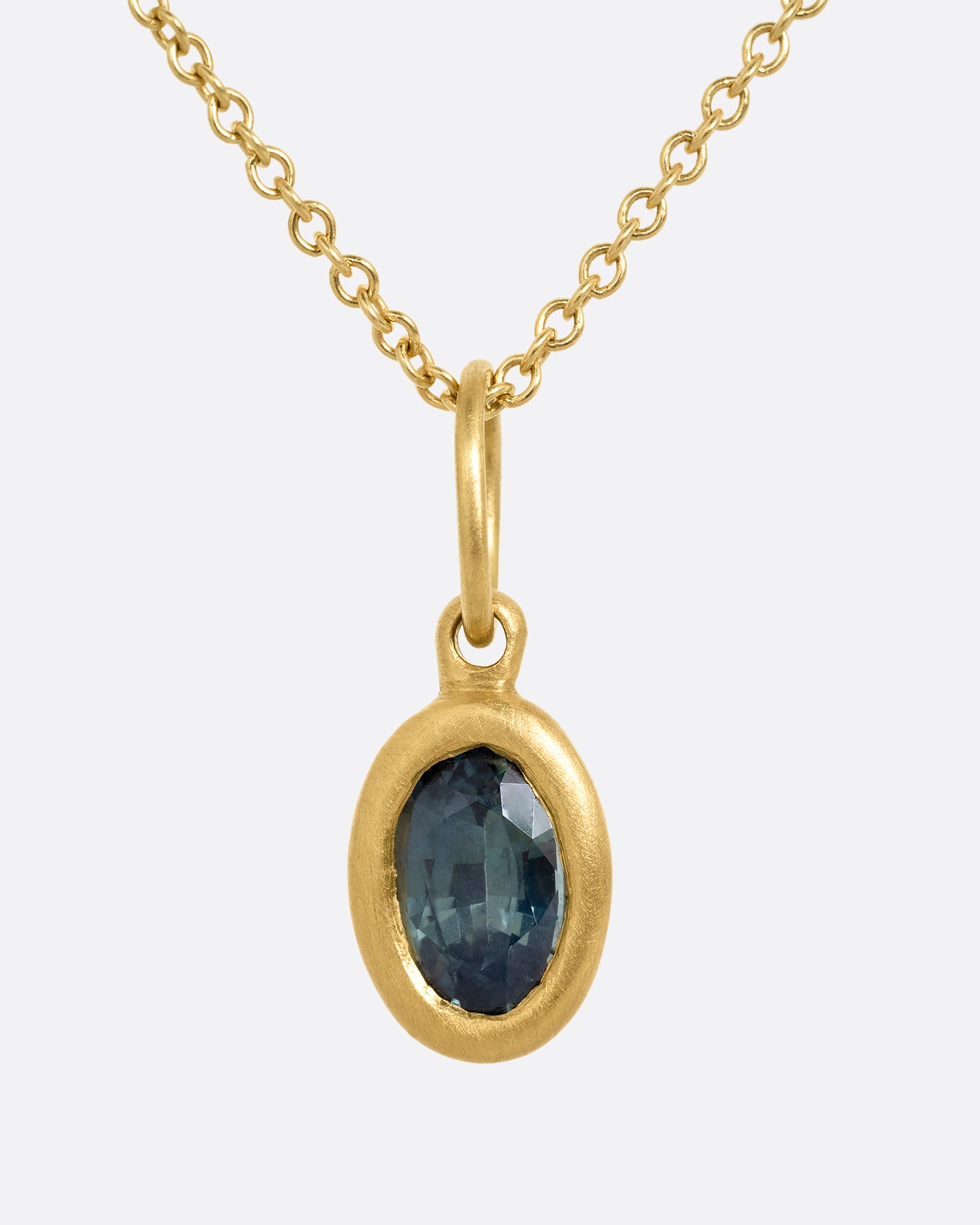 A yellow gold cable chain necklace with a bezel set oval blue green sapphire. Shown from the front.