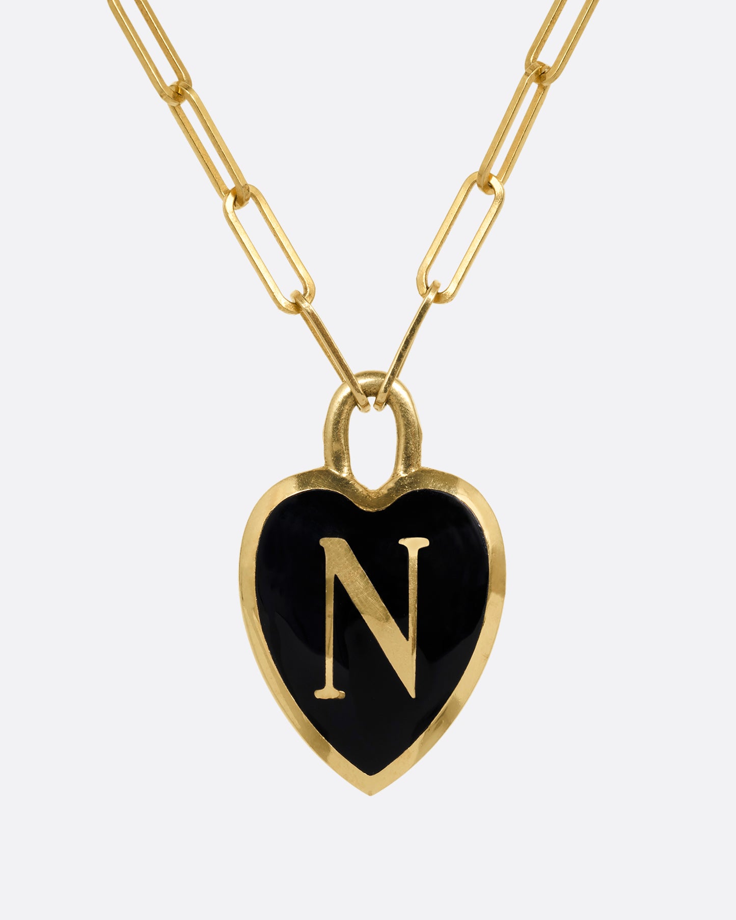 A yellow gold paperclip chain necklace with a black enamel heart shaped N pendant. Shown from the front.