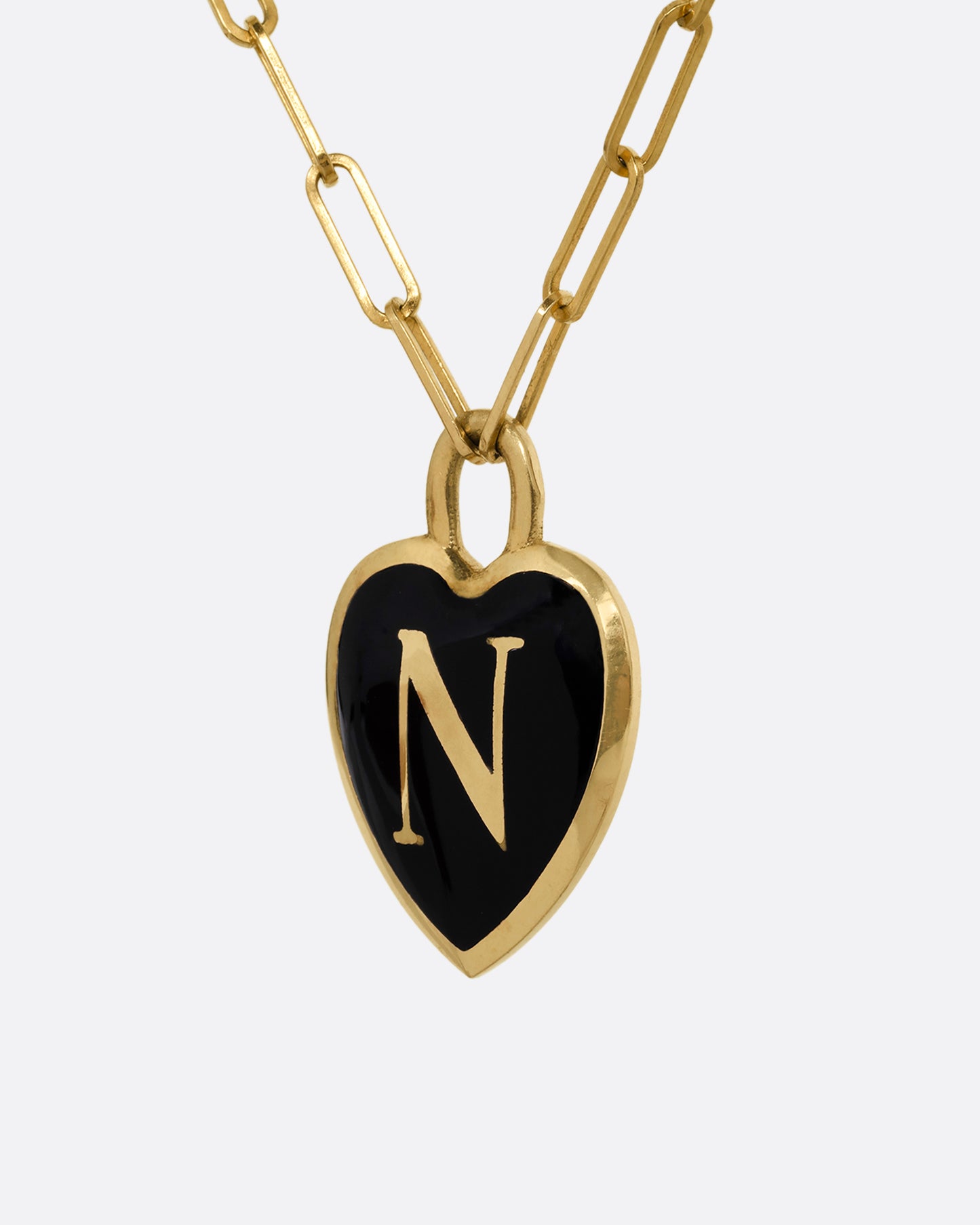 A yellow gold paperclip chain necklace with a black enamel heart shaped N pendant. Shown from the side.