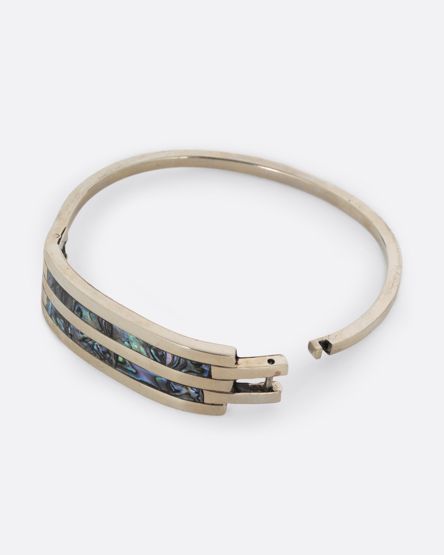 An alpaca silver bracelet with two abalone stripes and a hinged clasp. Shown open from the side.