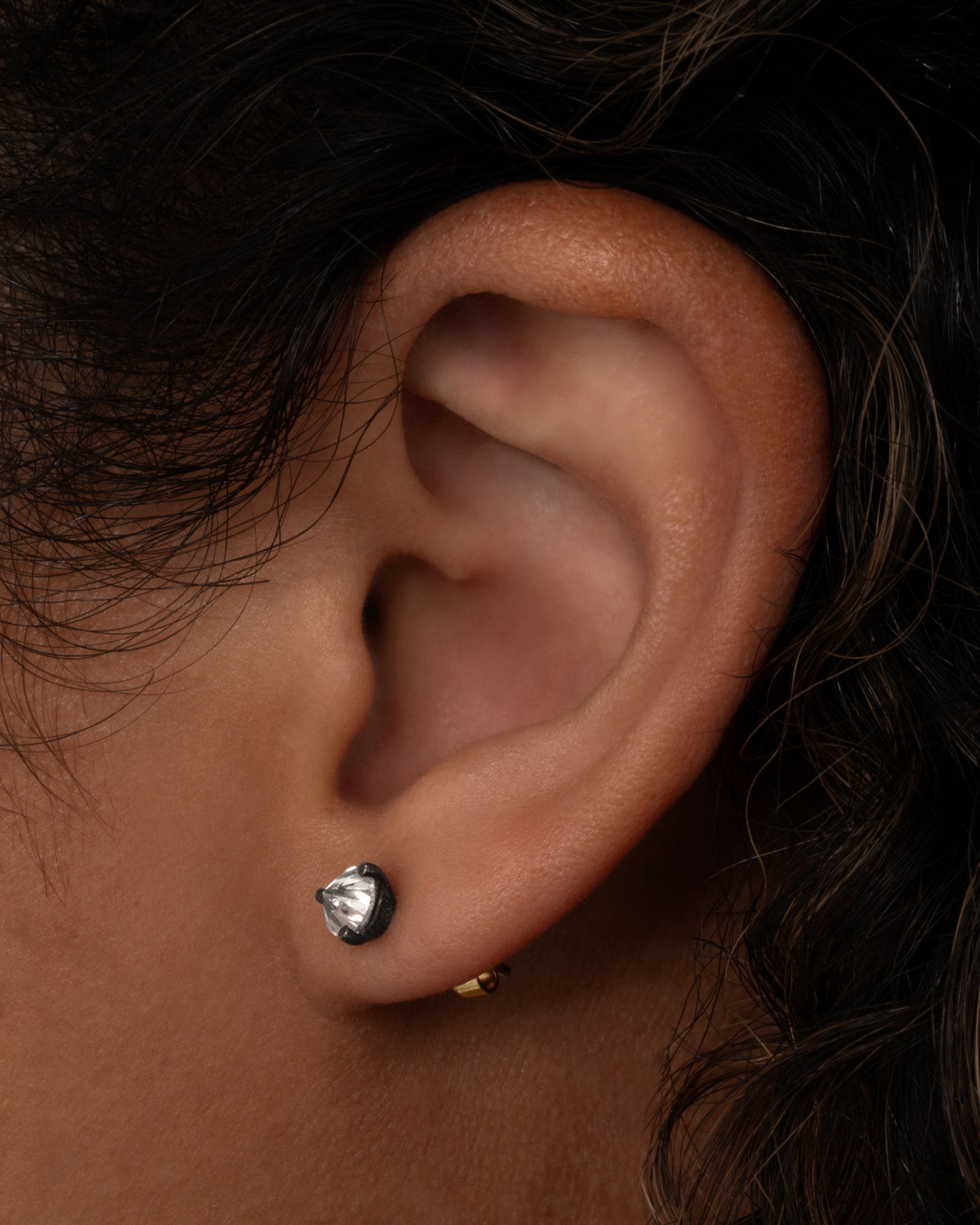 A pair of solitaire stud earrings with round inverted diamonds set in darkened white gold settings. Shown worn on an ear.