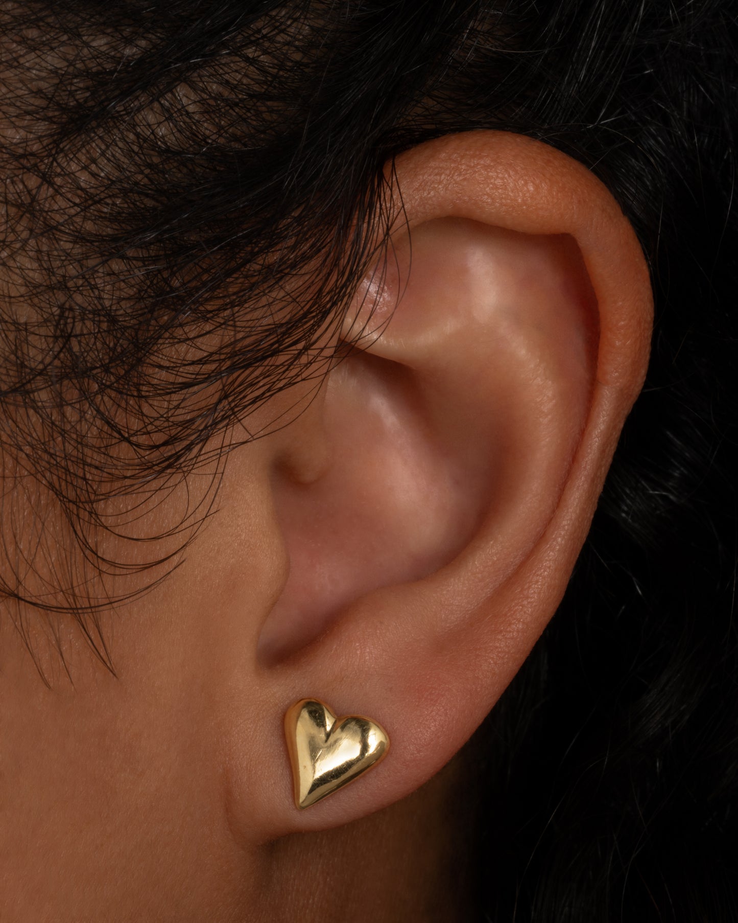 A yellow gold heart earring. Shown from the front on a person.