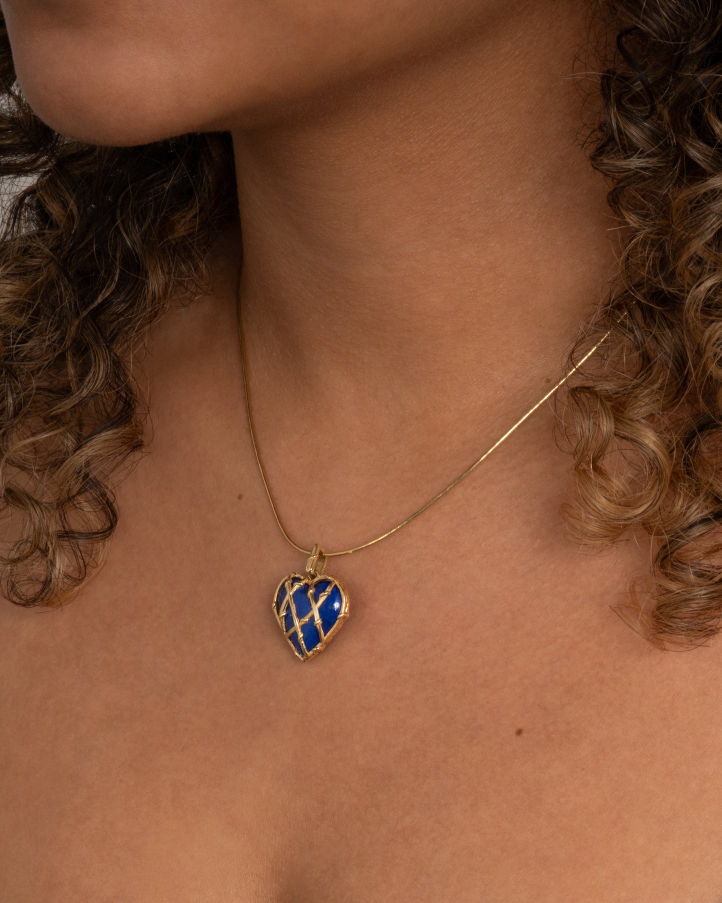 yellow gold heart shaped lapis charm shown worn on a snake chain around the neck