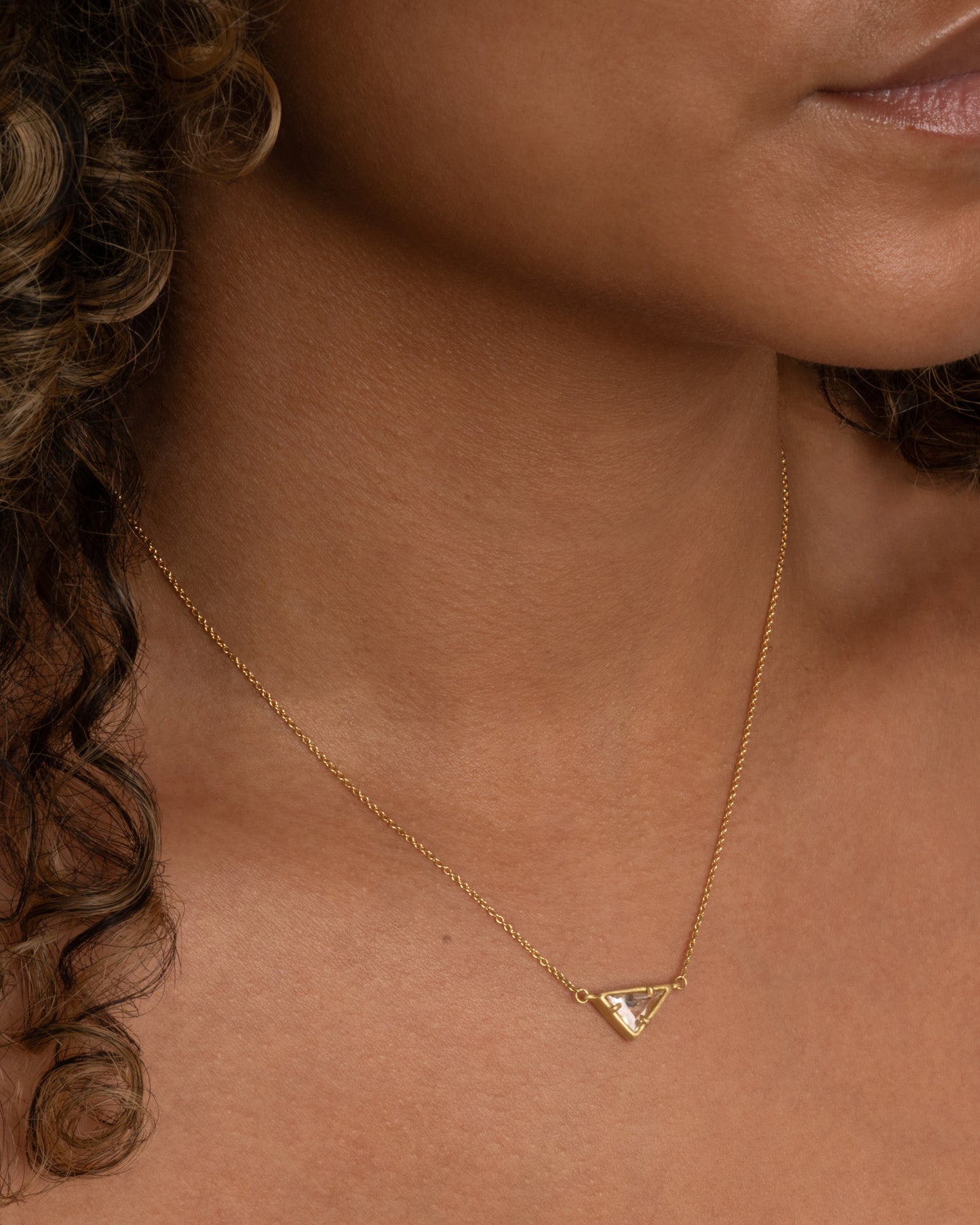 A yellow gold necklace with a triangular goshenite pendant. Shown worn around a neck.