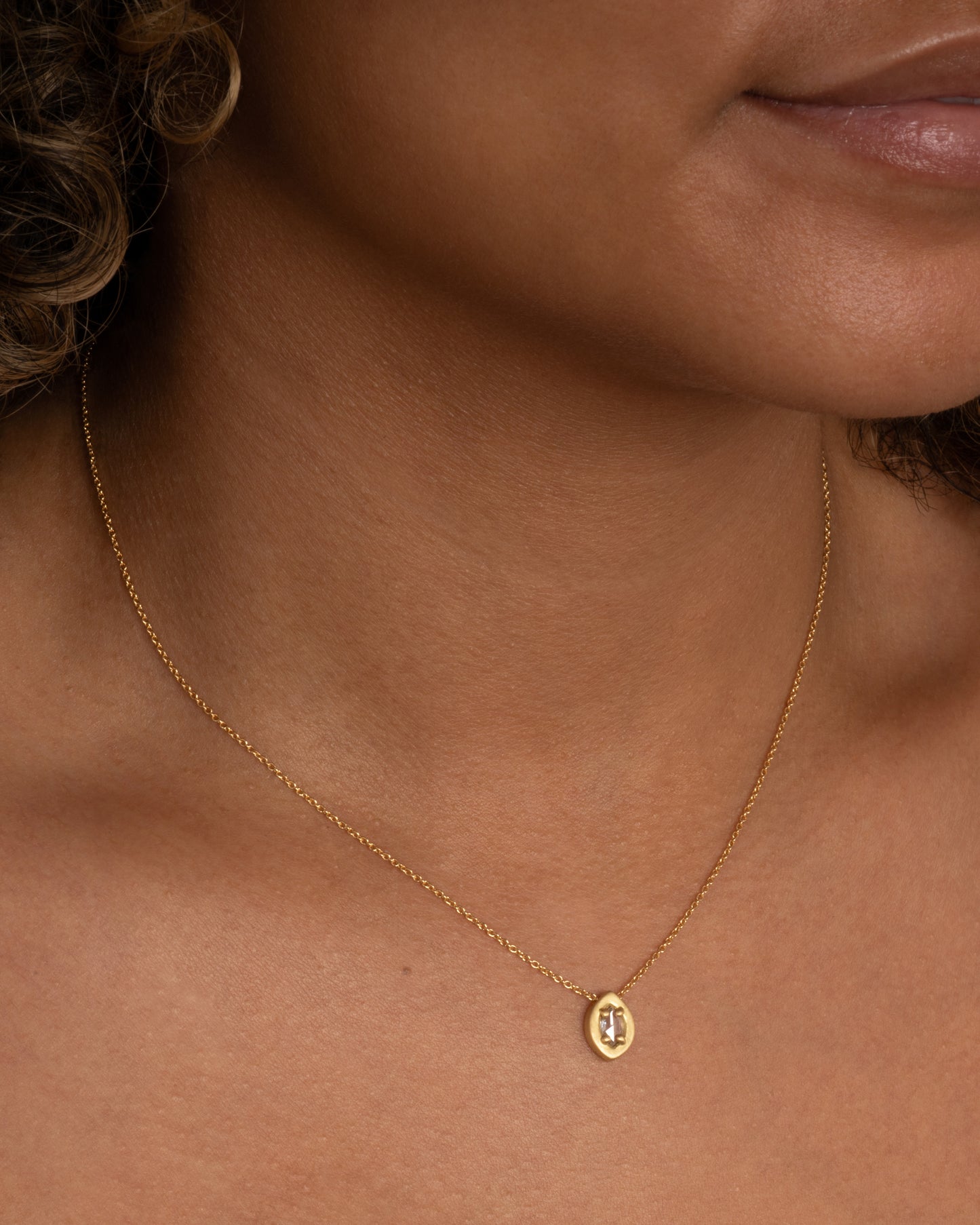 A yellow gold necklace with a prong set marquise diamond pendant. Shown worn around a neck.