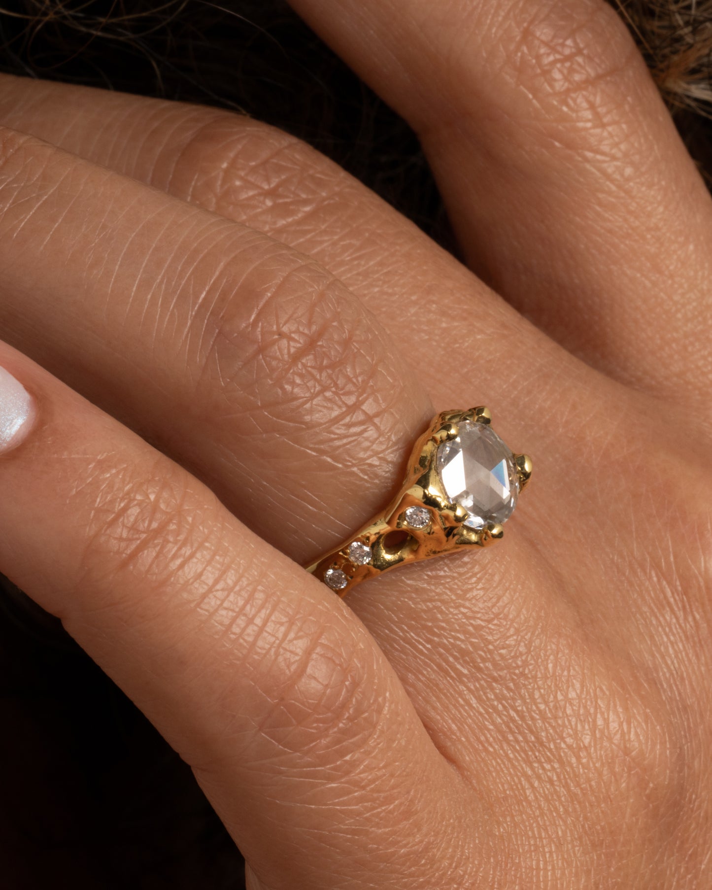A yellow gold ring with a rose cut diamond, cutouts, and diamond details. Shown on a hand from the side.
