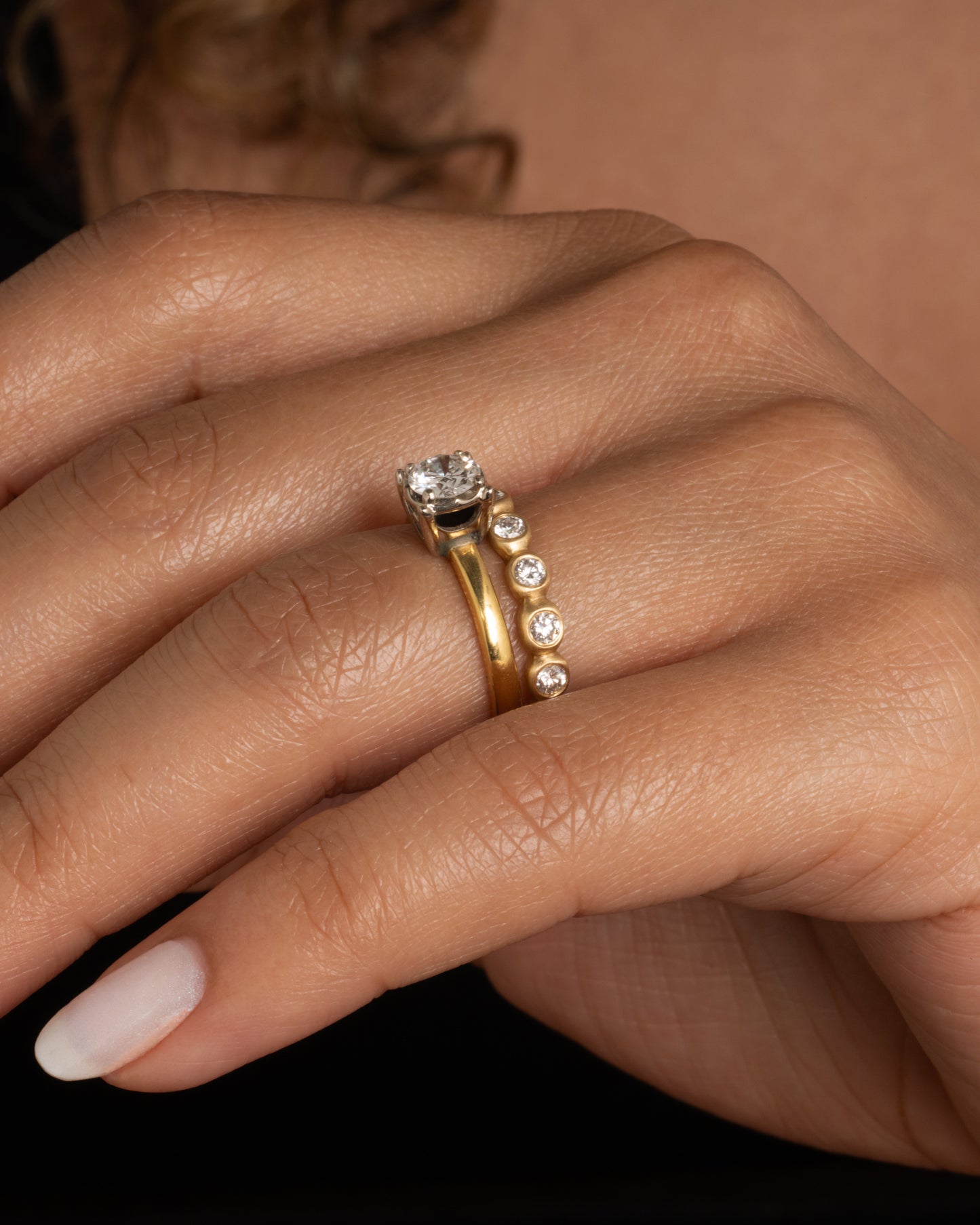 A yellow gold eternity band of bezel set white diamonds. Shown worn on a finger paired with a vintage engagement ring.