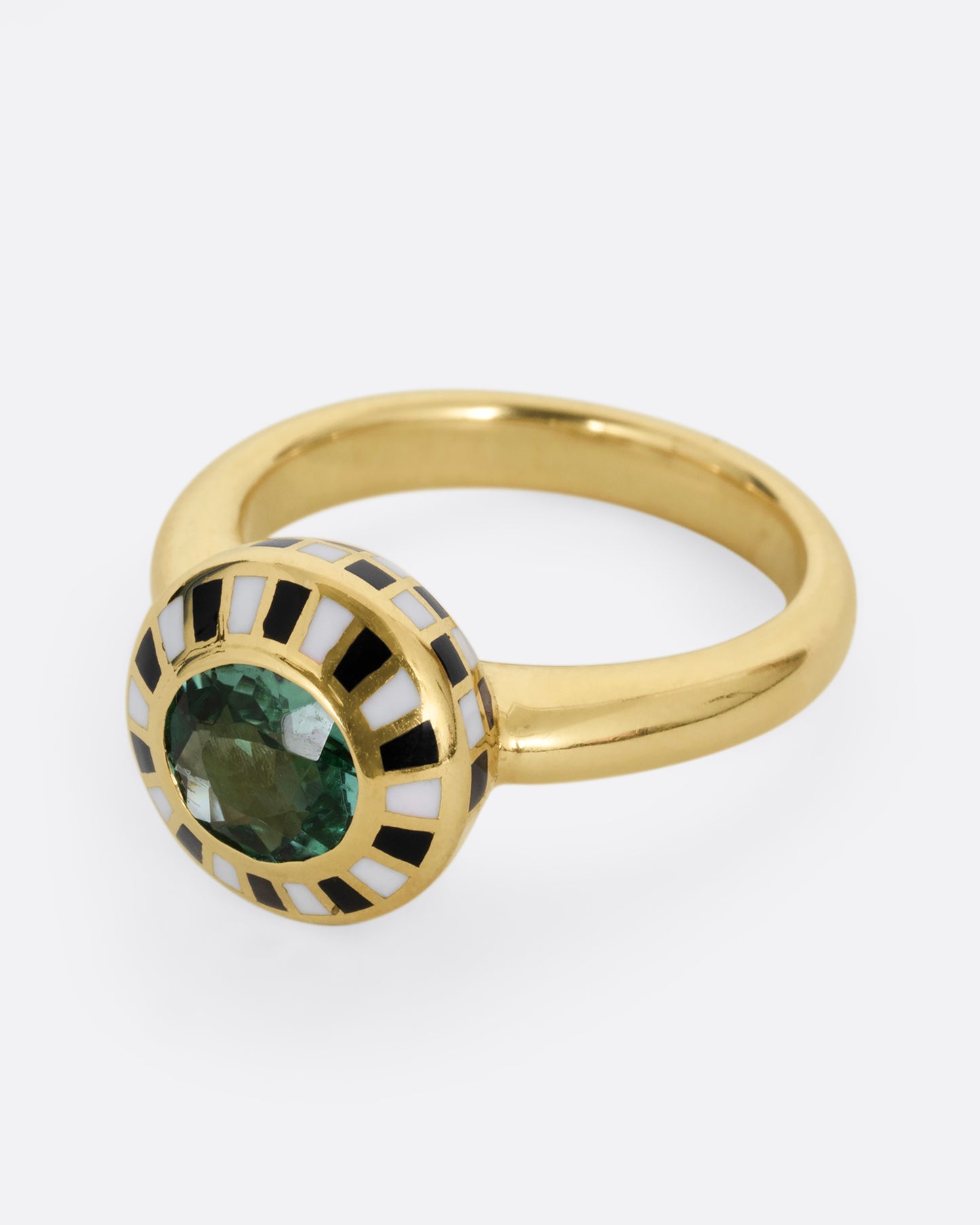 A yellow gold ring with an enamel black and white checkerboard pattern framing a green tourmaline. Shown from the side.