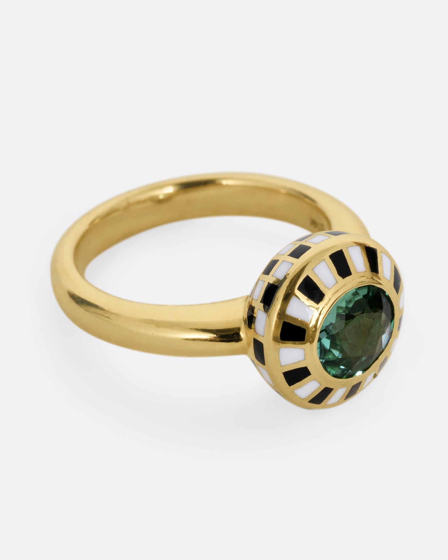 A yellow gold ring with an enamel black and white checkerboard pattern framing a green tourmaline. Shown from the side.
