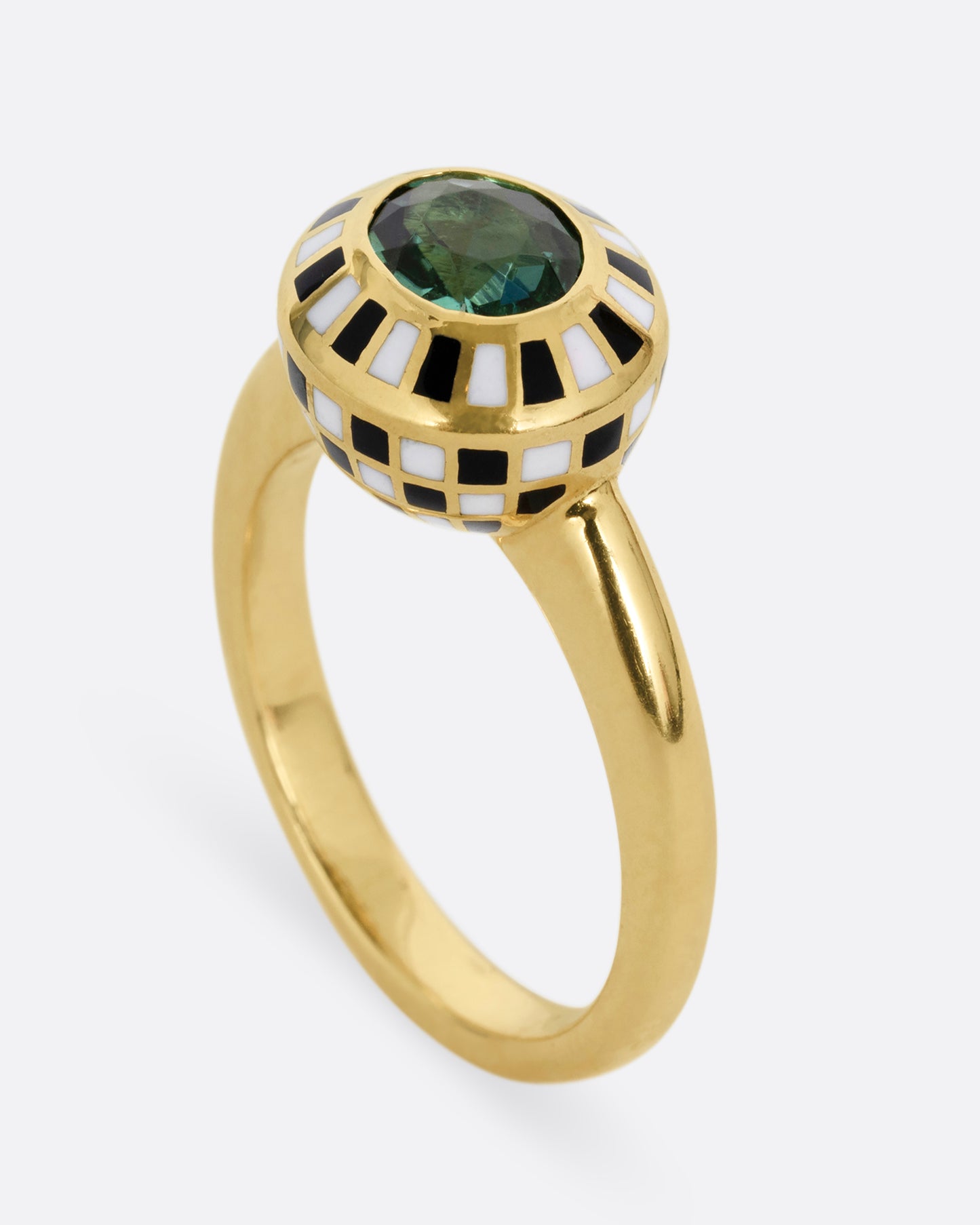 A yellow gold ring with an enamel black and white checkerboard pattern framing a green tourmaline. Shown standing up from the side.