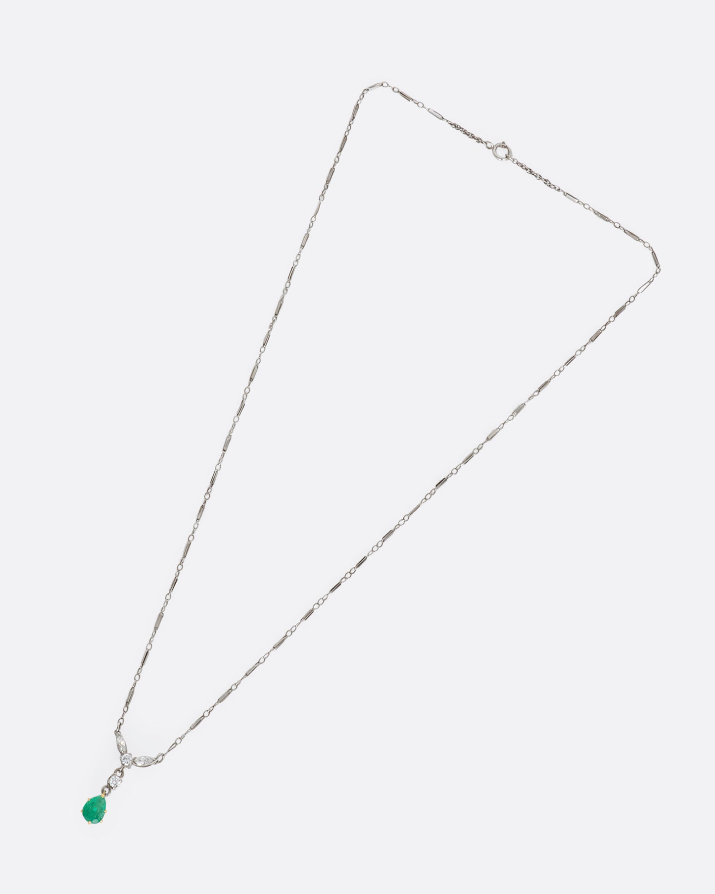 White gold necklace featuring diamonds and an emerald at the center. View from above, lying flat.