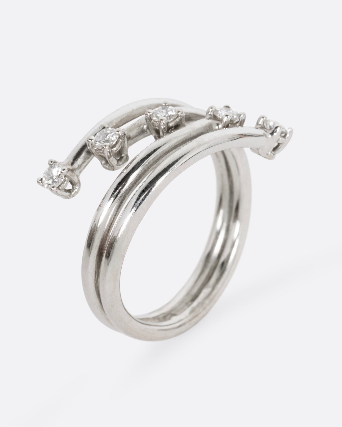 A white gold wrap ring with five diagonal prong set diamonds, shown from the side standing up.