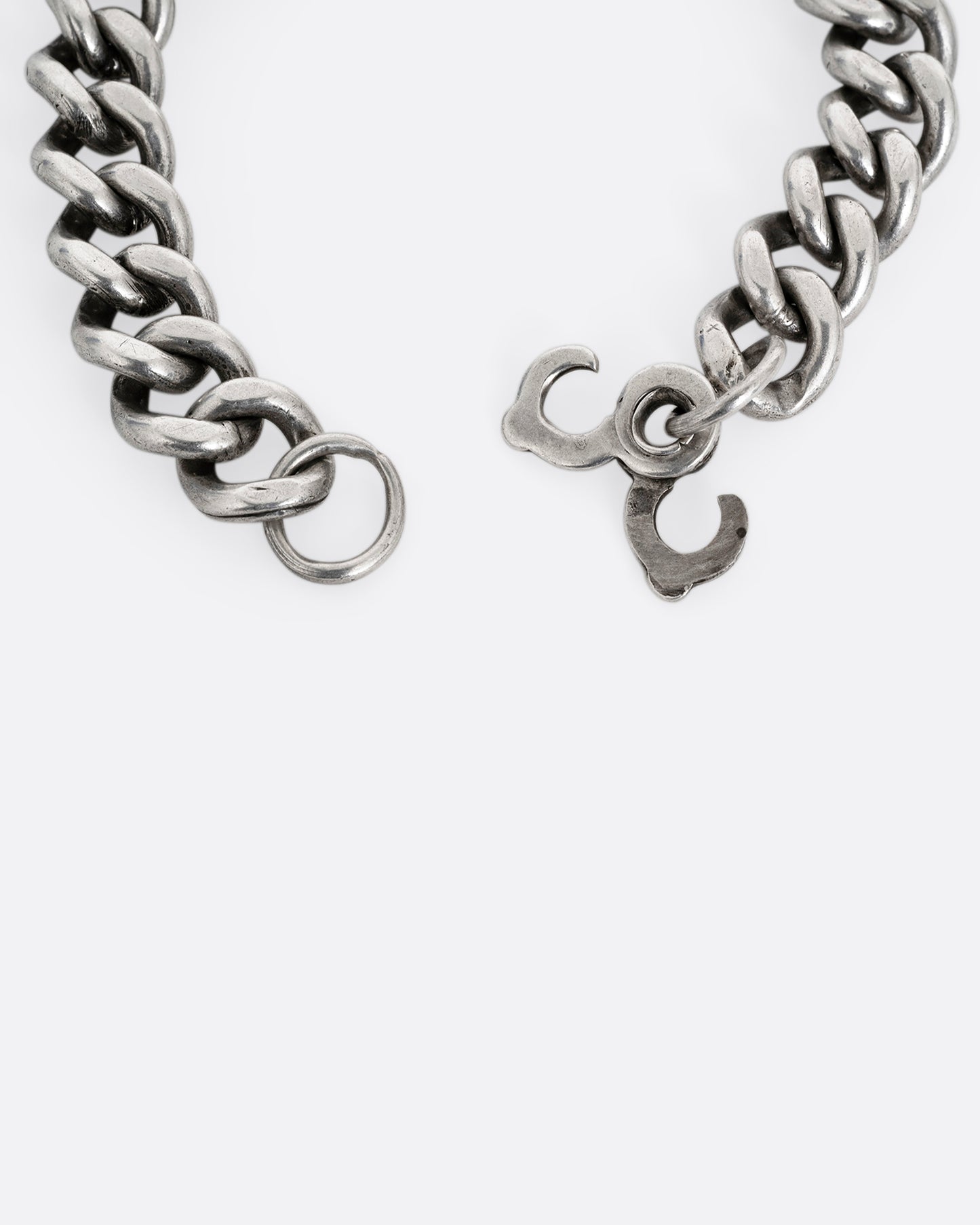 A close up of the clasp of a silver curb chain ID bracelet, shown from the back open.