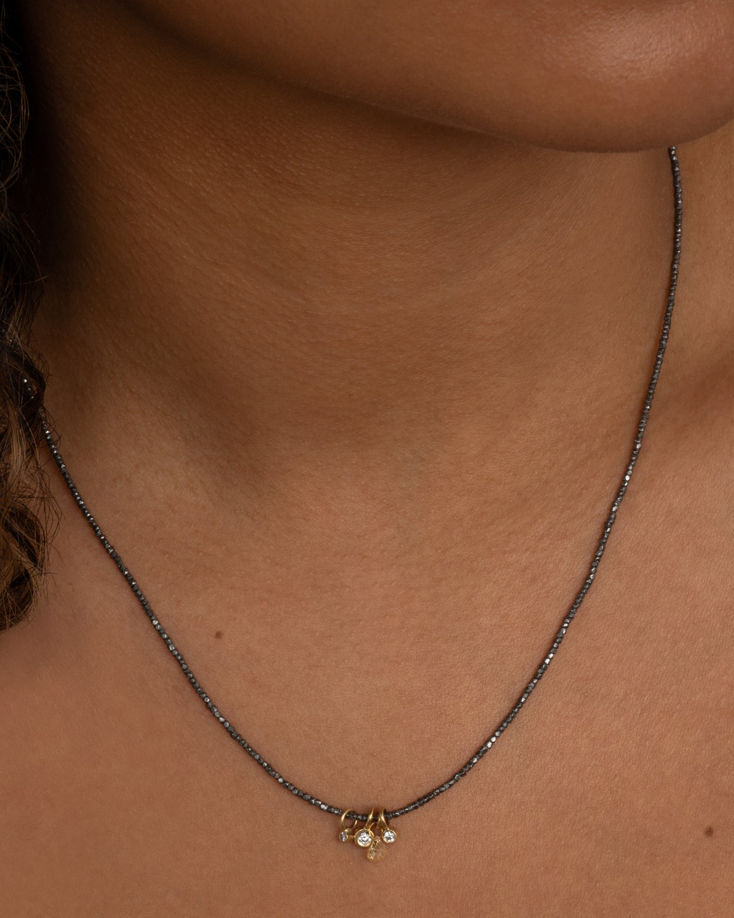 An oxidized silver beaded necklace with four different diamond charms. Shown worn around the neck.