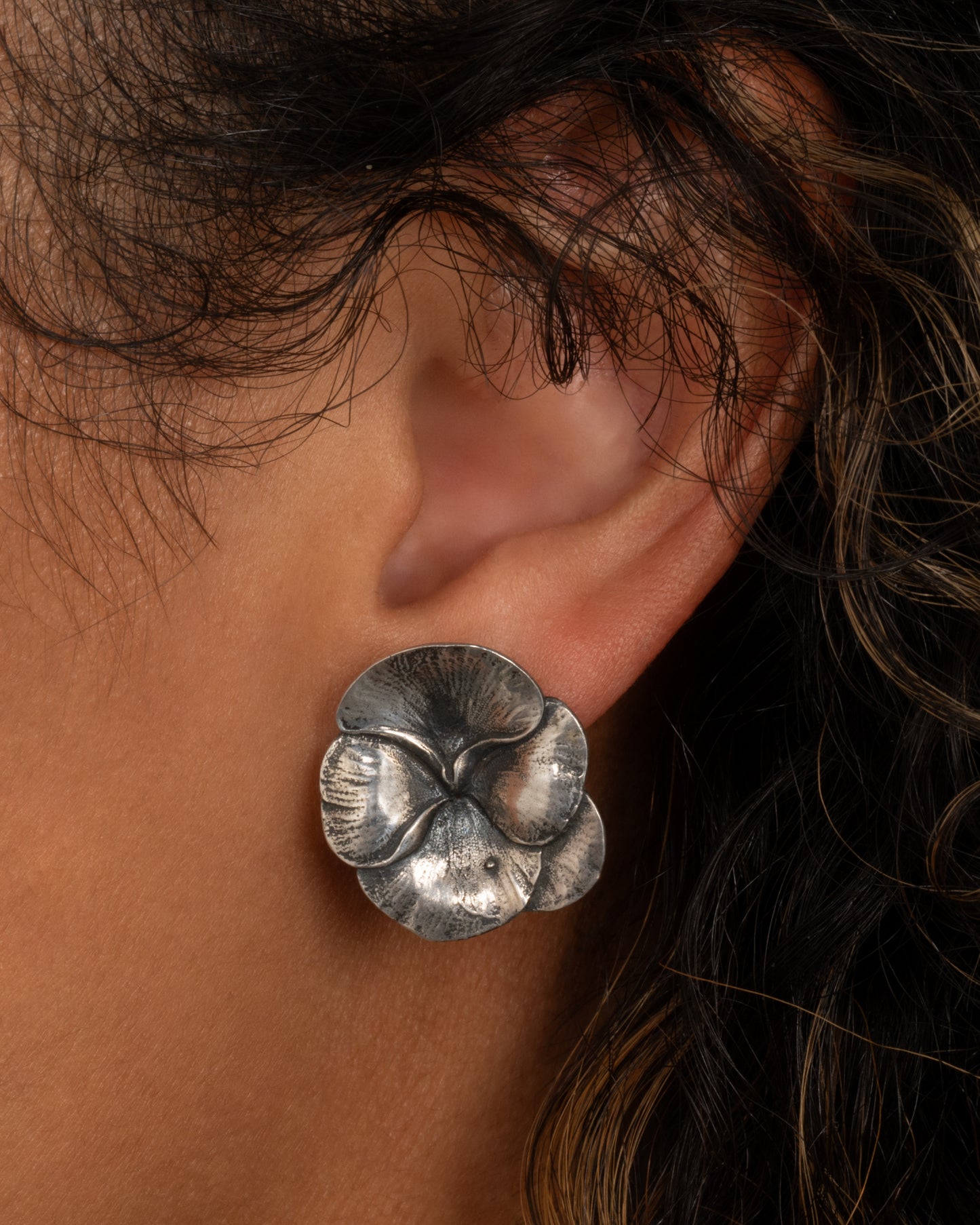 A silver pansy earring, shown from the front on a person.