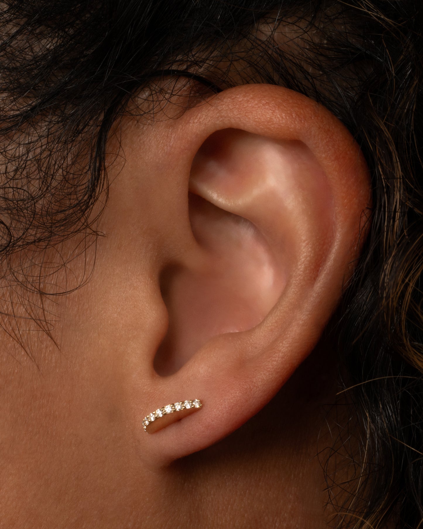 A half moon yellow gold stud with a diamond studded edge, shown in an ear.