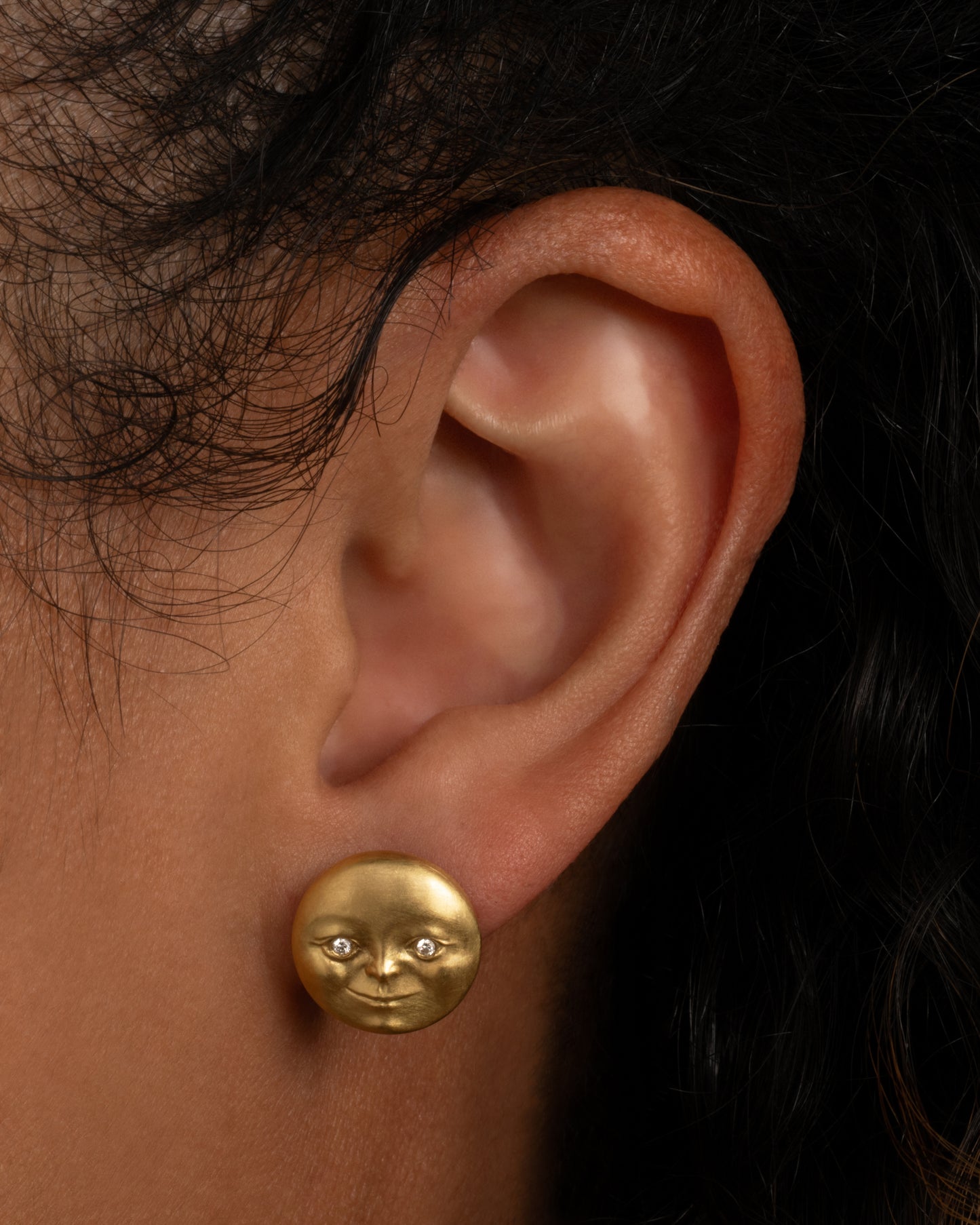 A yellow gold moon face stud earring with diamond eyes. Shown from the front on a person.