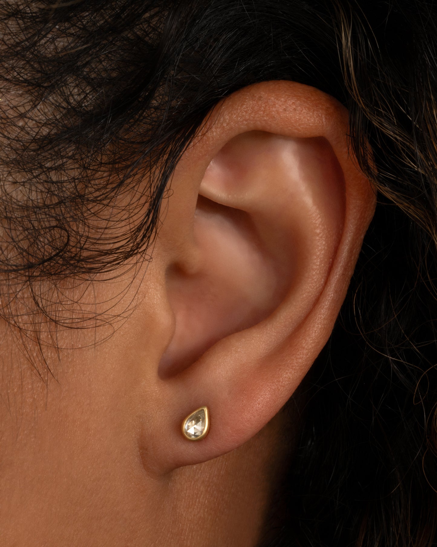 A yellow gold tear drop shaped stud earring with a diamond. Shown from the front on a person.