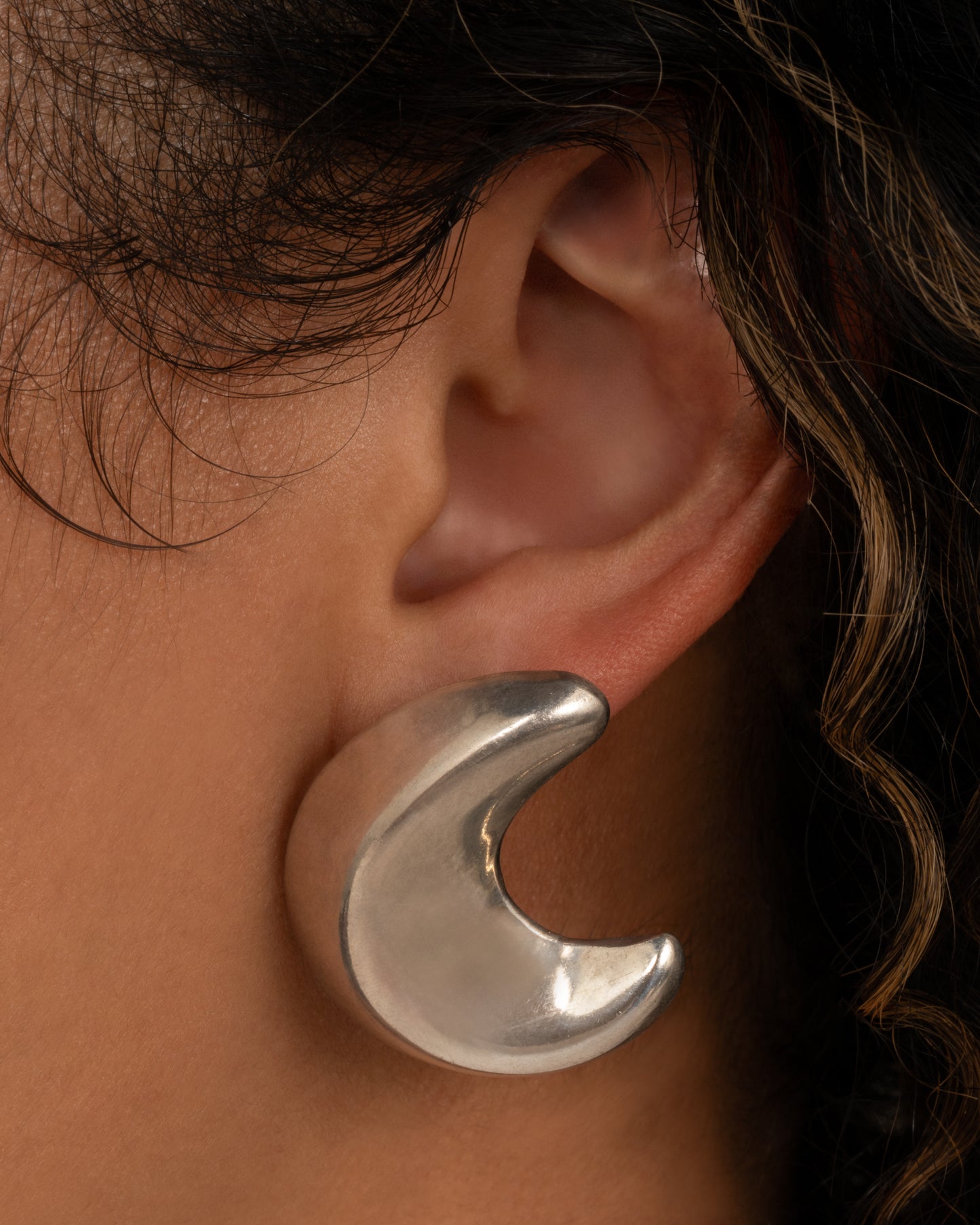 A silver crescent moon-shaped stud earring, shown from the front on a person.