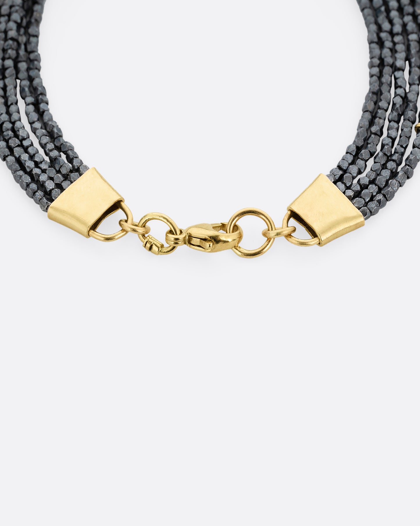 A close up of a bracelet with five strands of oxidized silver beads converging at yellow gold capped ends with a lobster clasp. Shown from the top.