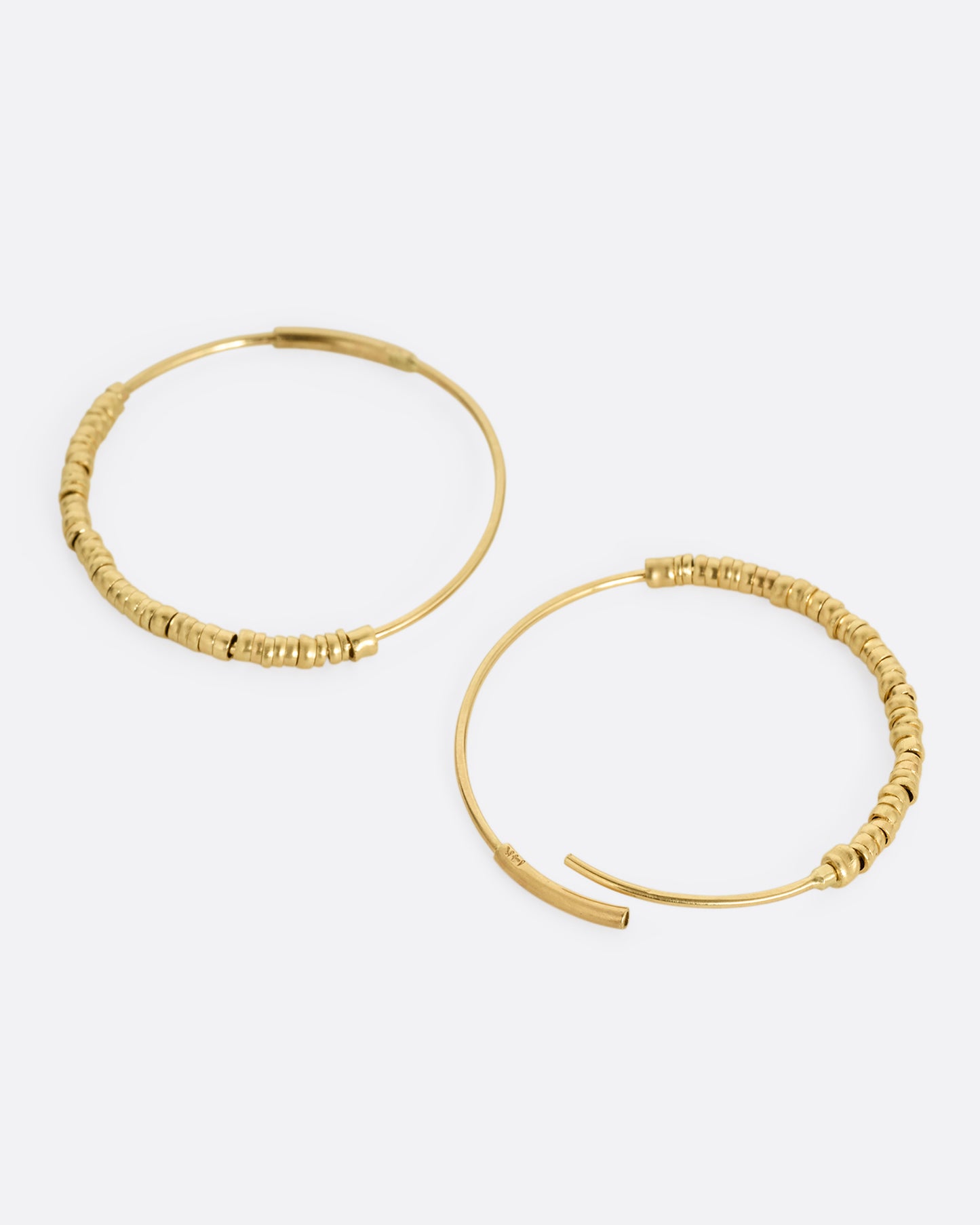 A pair of yellow gold hoop earrings with freely moving beads. Shown lying flat from the side with one hoop open.