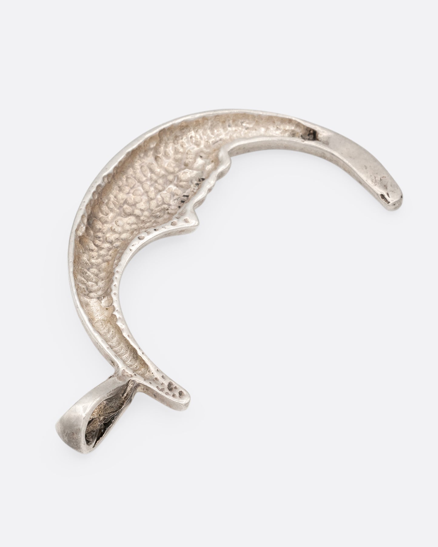 A silver crescent moon charm with a face. Shown from the back lying flat.