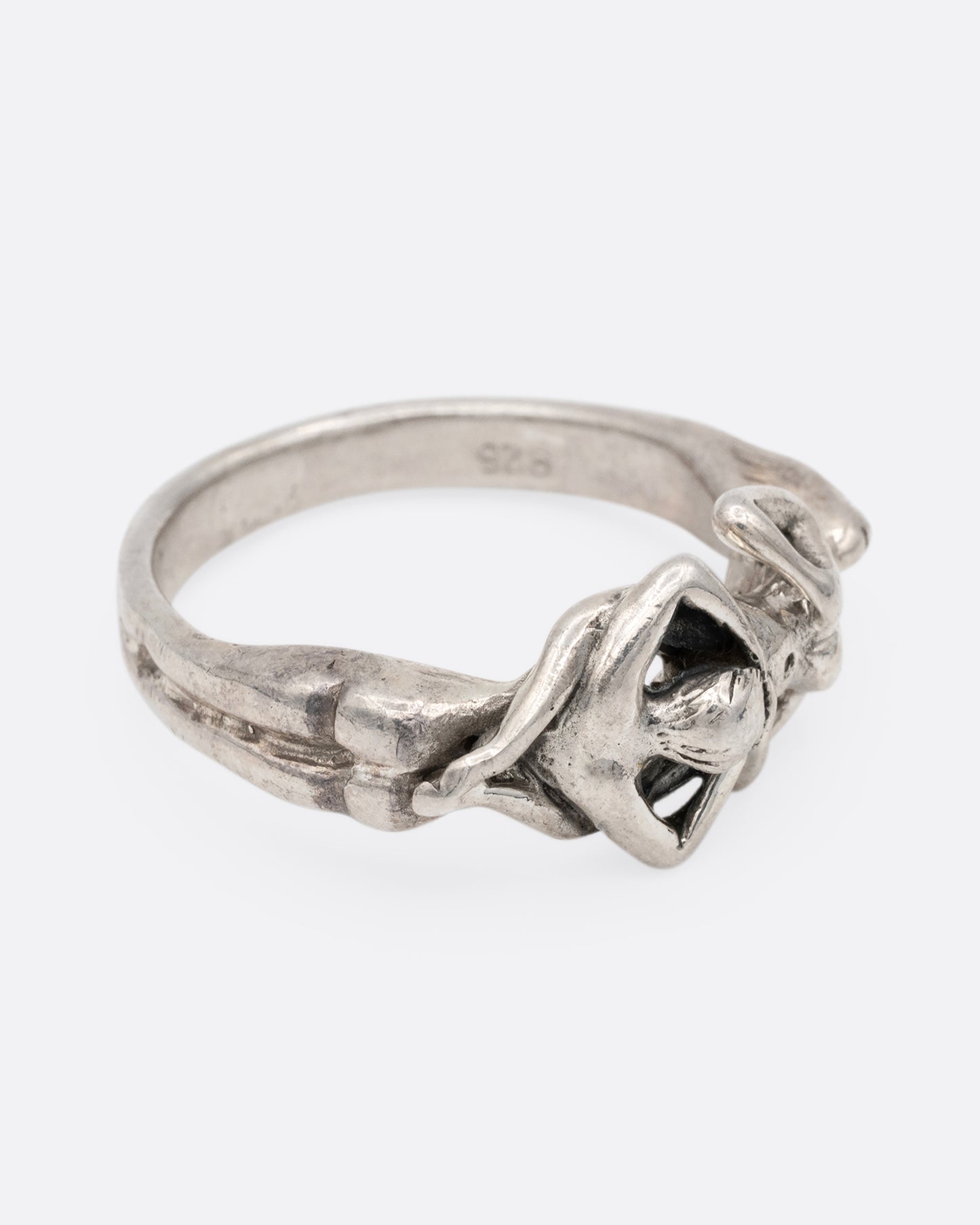 A silver ring with an erotic couple. Shown from the side.