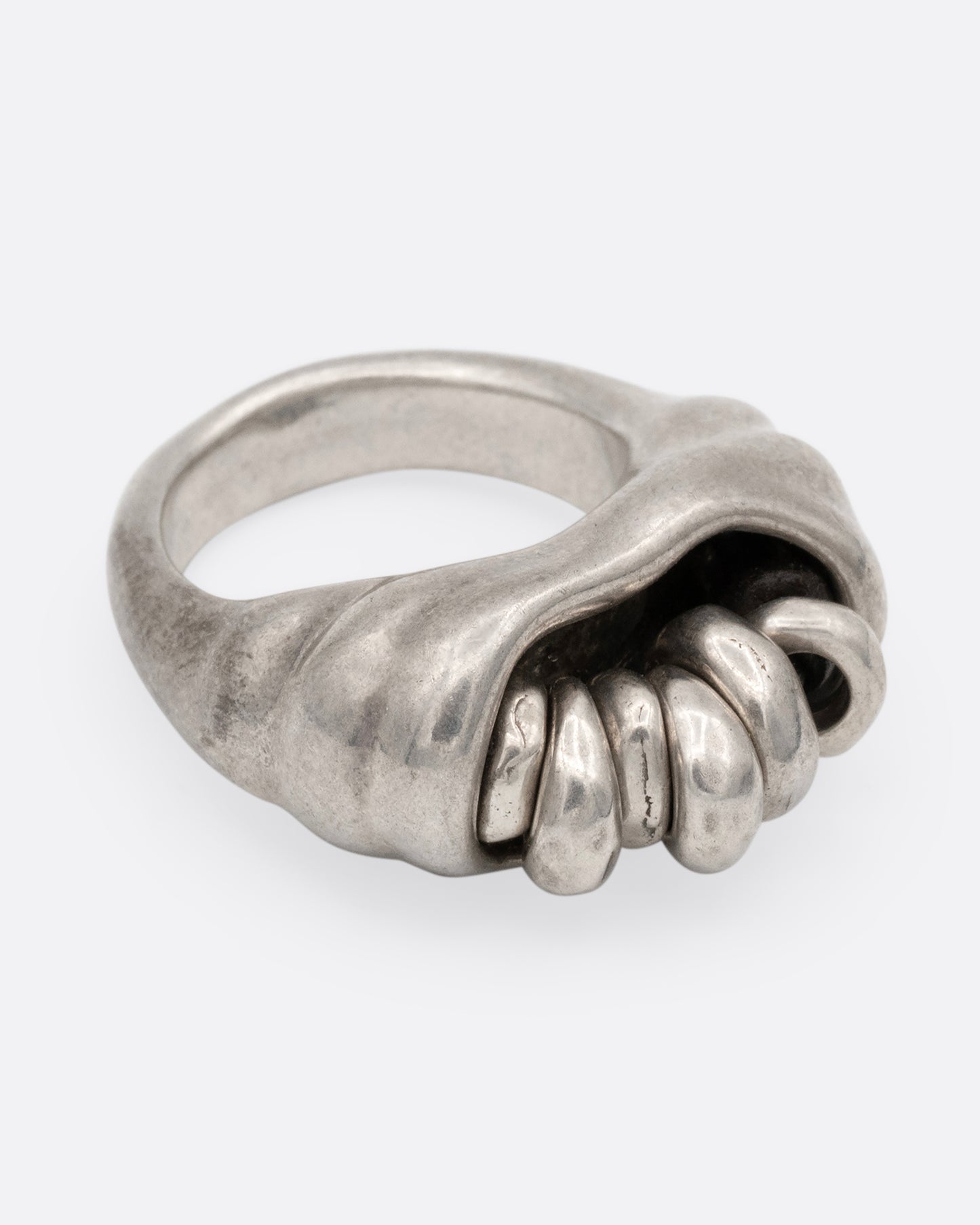 A silver ring with a cluster of free moving hoops nestled into its towering face. Shown from the side.