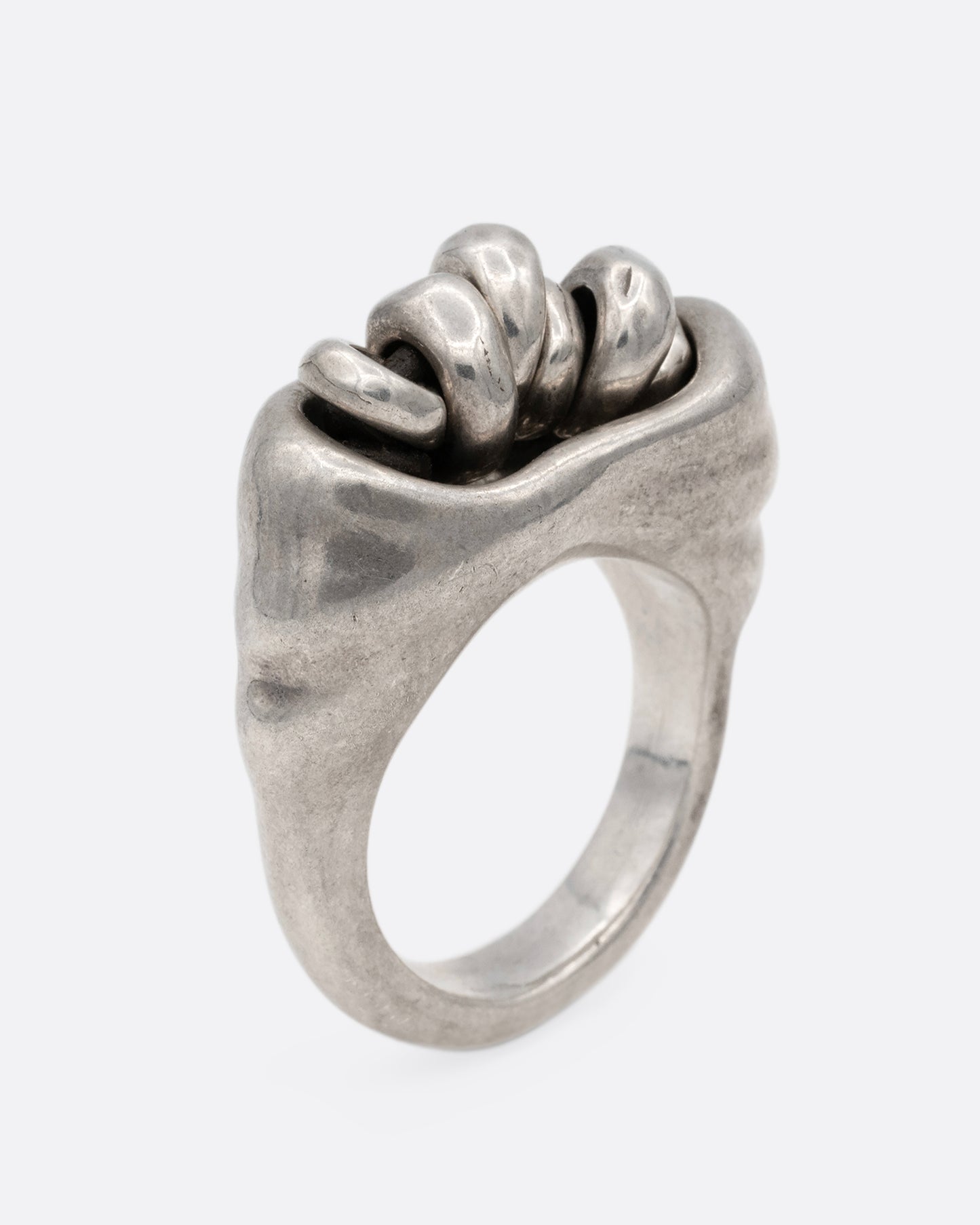 A silver ring with a cluster of free moving hoops nestled into its towering face. Shown standing up from the side.