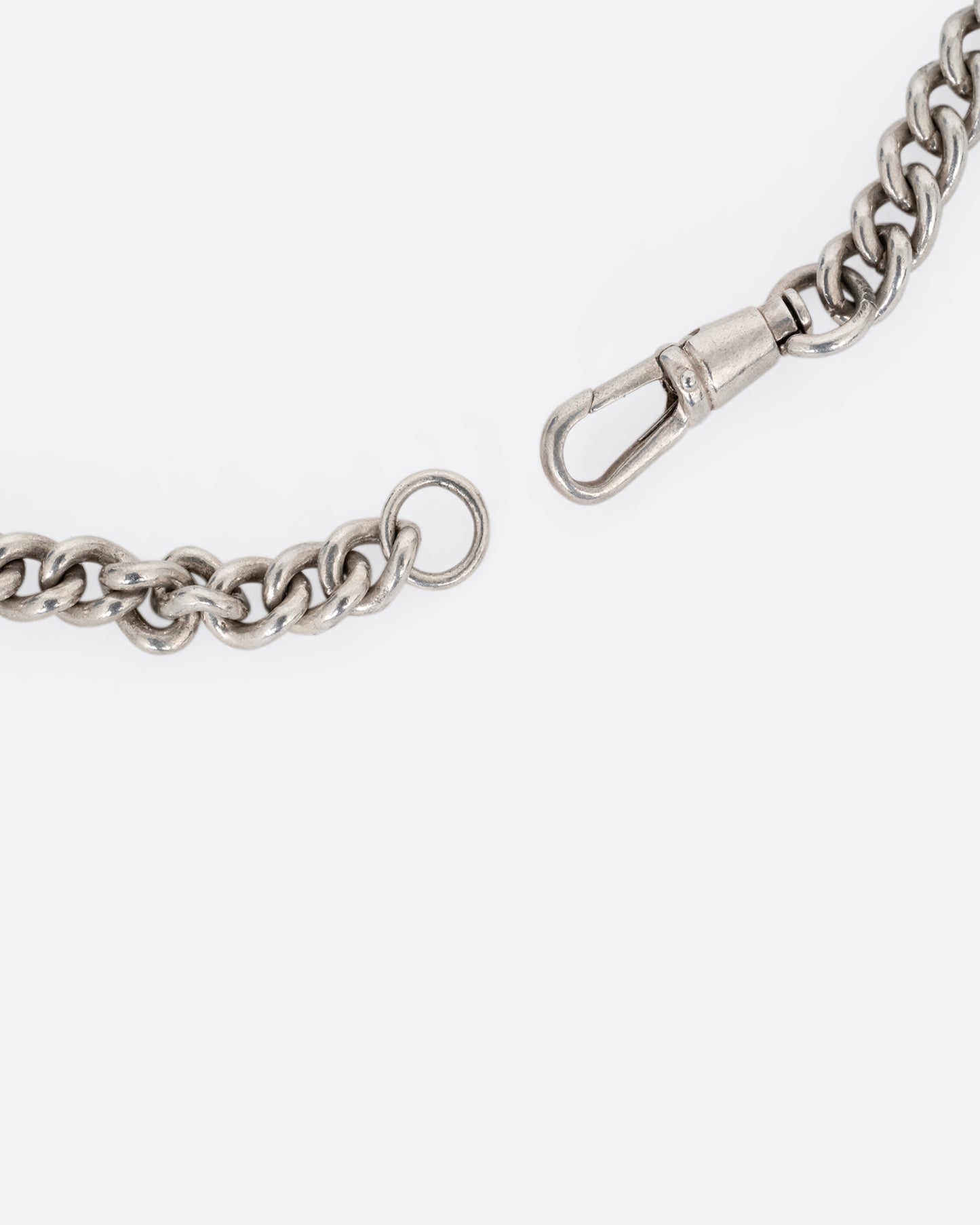 A close up of a silver curb chain pocket watch curb chain necklace with a T-bar on one end.