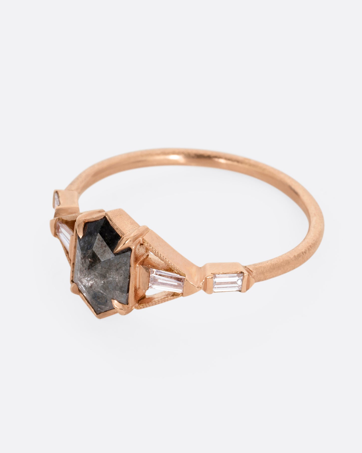 A rose gold ring with a black hexagonal diamond and baguette diamond lined shoulders. Shown from the side.