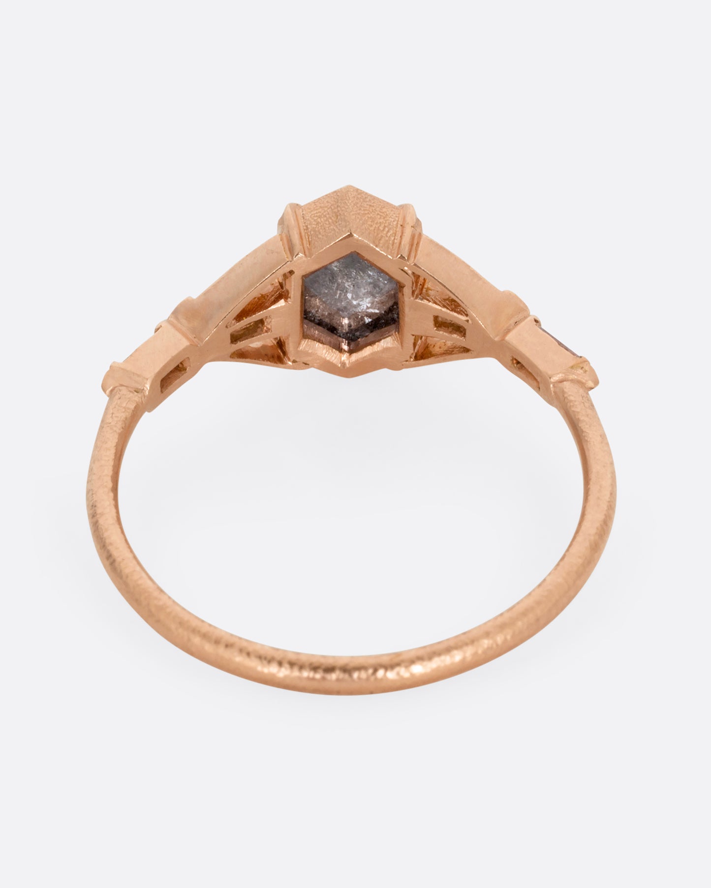 A rose gold ring with a black hexagonal diamond and baguette diamond lined shoulders. Shown from the back.