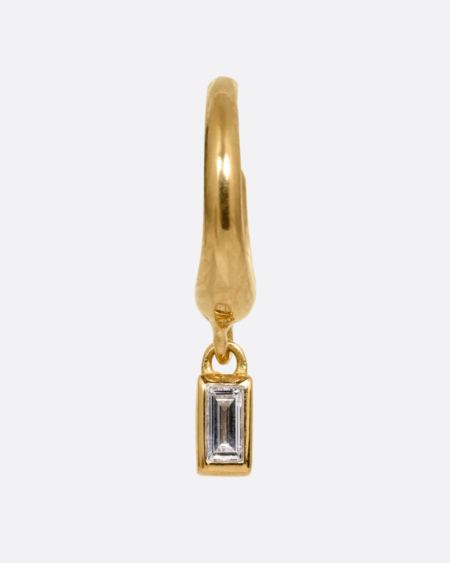 A yellow gold huggie hoop earring with a baguette diamond dangle. Shown from the front.