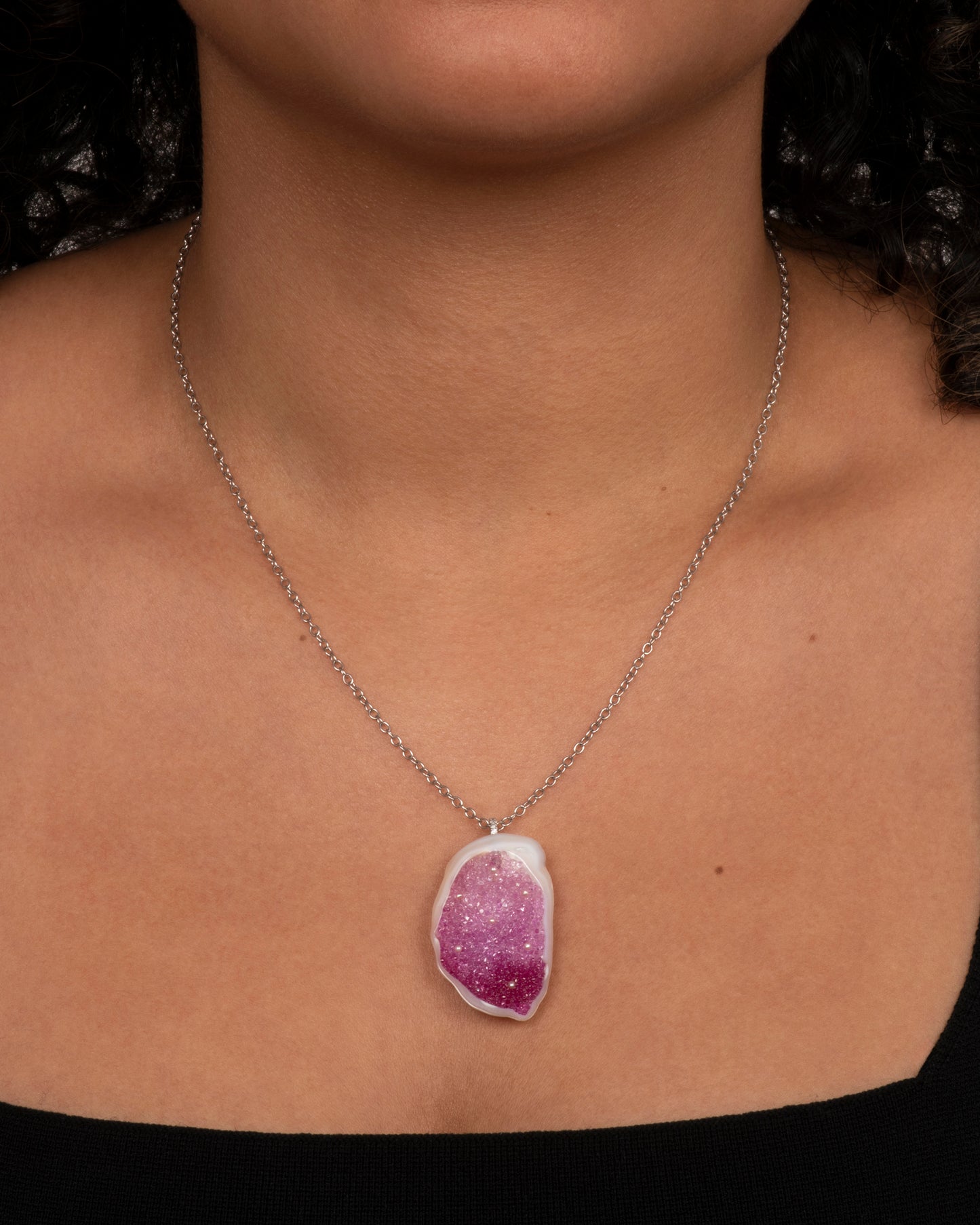 A large freshwater souffle pearl carved out and lined with ombre pink sapphires and seed pearls. It has a pave diamond lined bail and white gold cable chain. Shown from the front on a person.