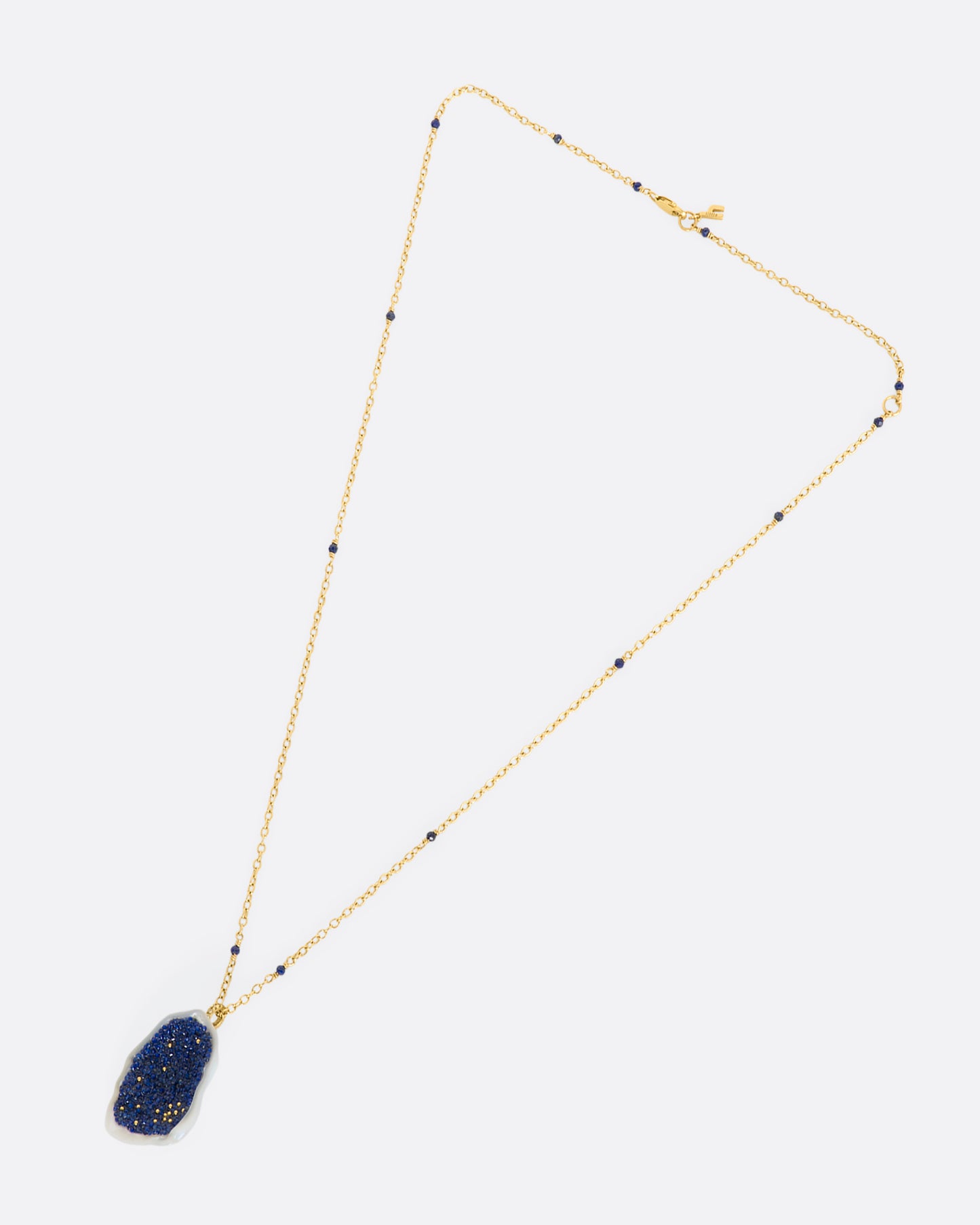 A yellow gold necklace with a hollowed out pearl pendant filled with lapis and 22k gold beads. Shown laying flat.