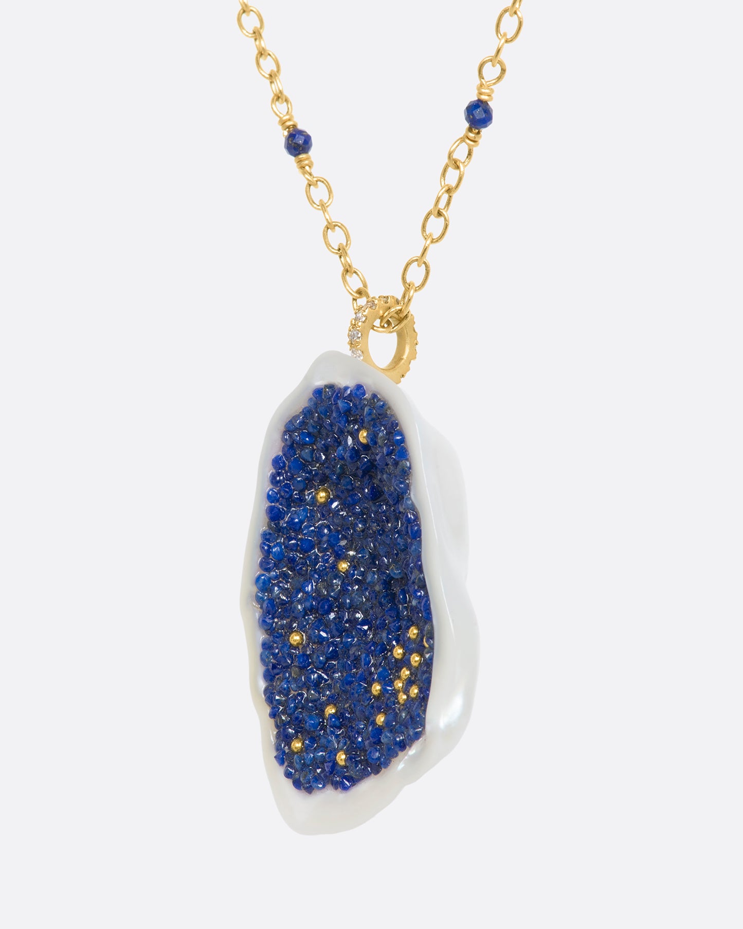 A yellow gold necklace with a hollowed out pearl pendant filled with lapis and 22k gold beads. Shown from the side.