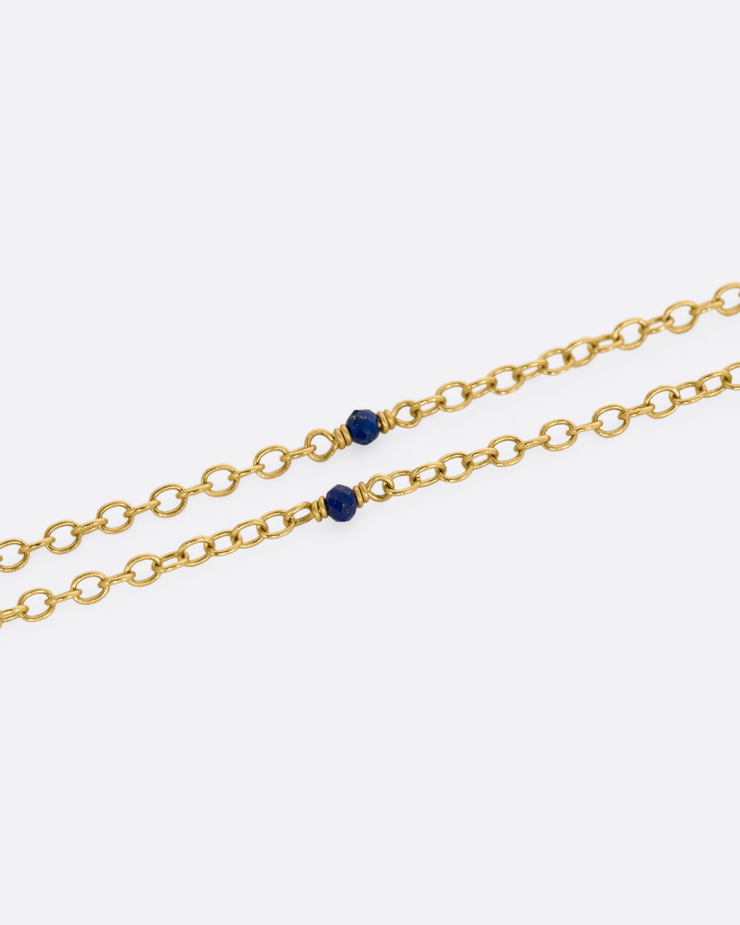 A yellow gold necklace with a hollowed out pearl pendant filled with lapis and 22k gold beads. Shown close up of the lapis beads on the chain.