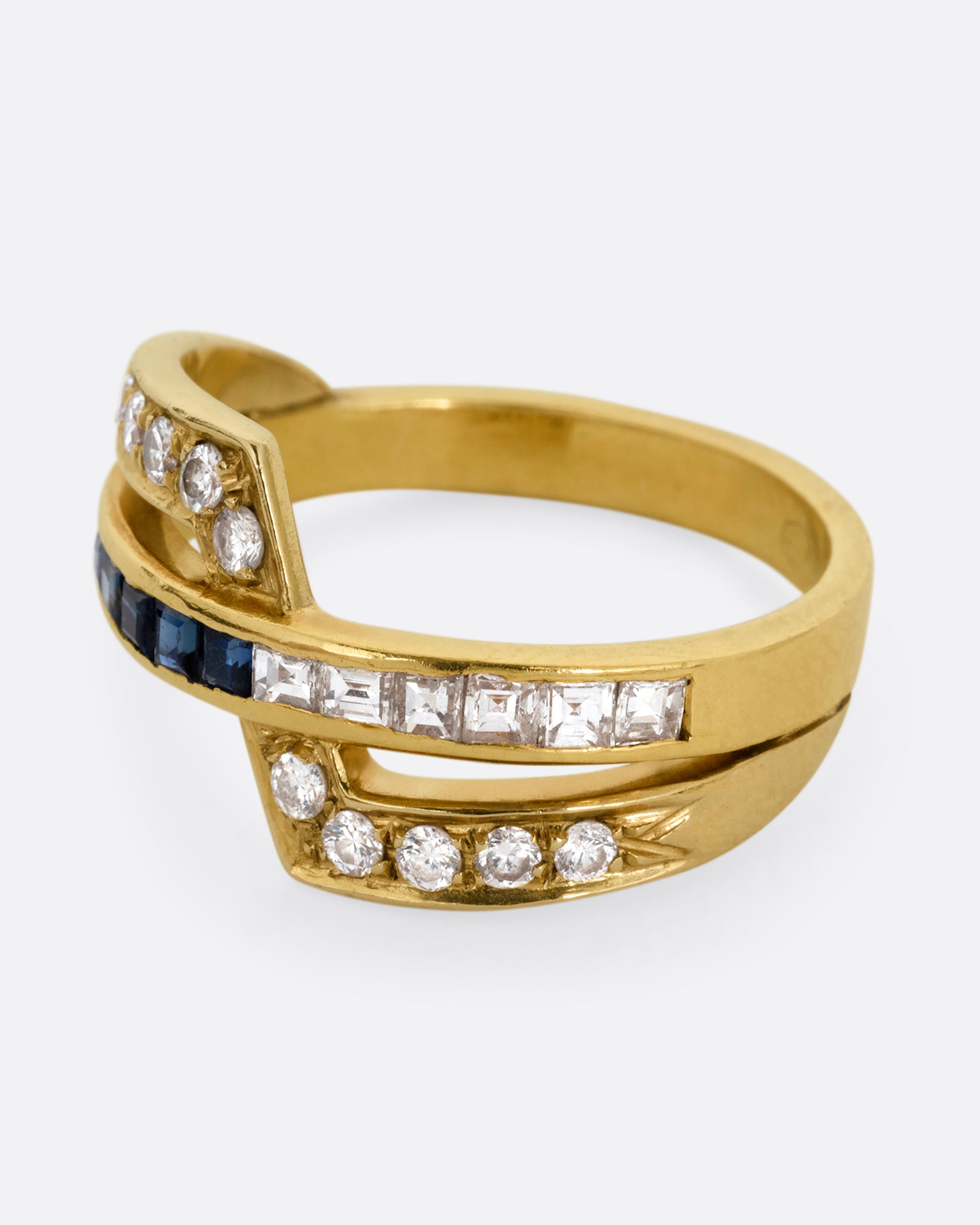 A yellow gold ring with an intersection of diamonds and blue sapphires. Shown from the side.