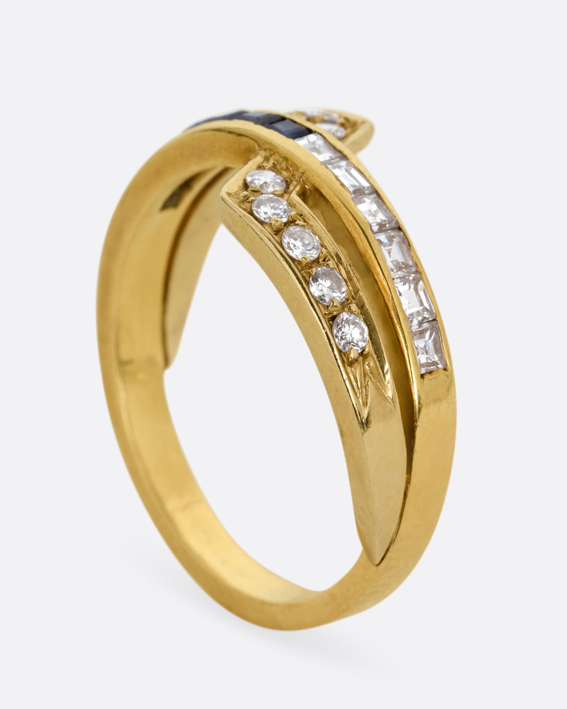 A yellow gold ring with an intersection of diamonds and blue sapphires. Shown from the side standing up.