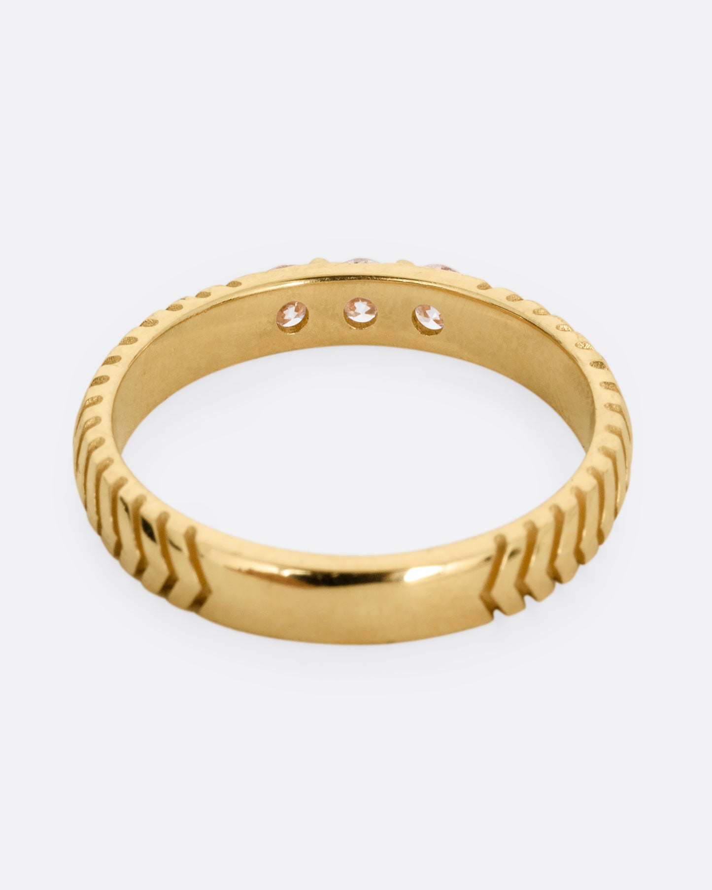A yellow gold ring with arrow etching and three white diamonds. Shown from the back.