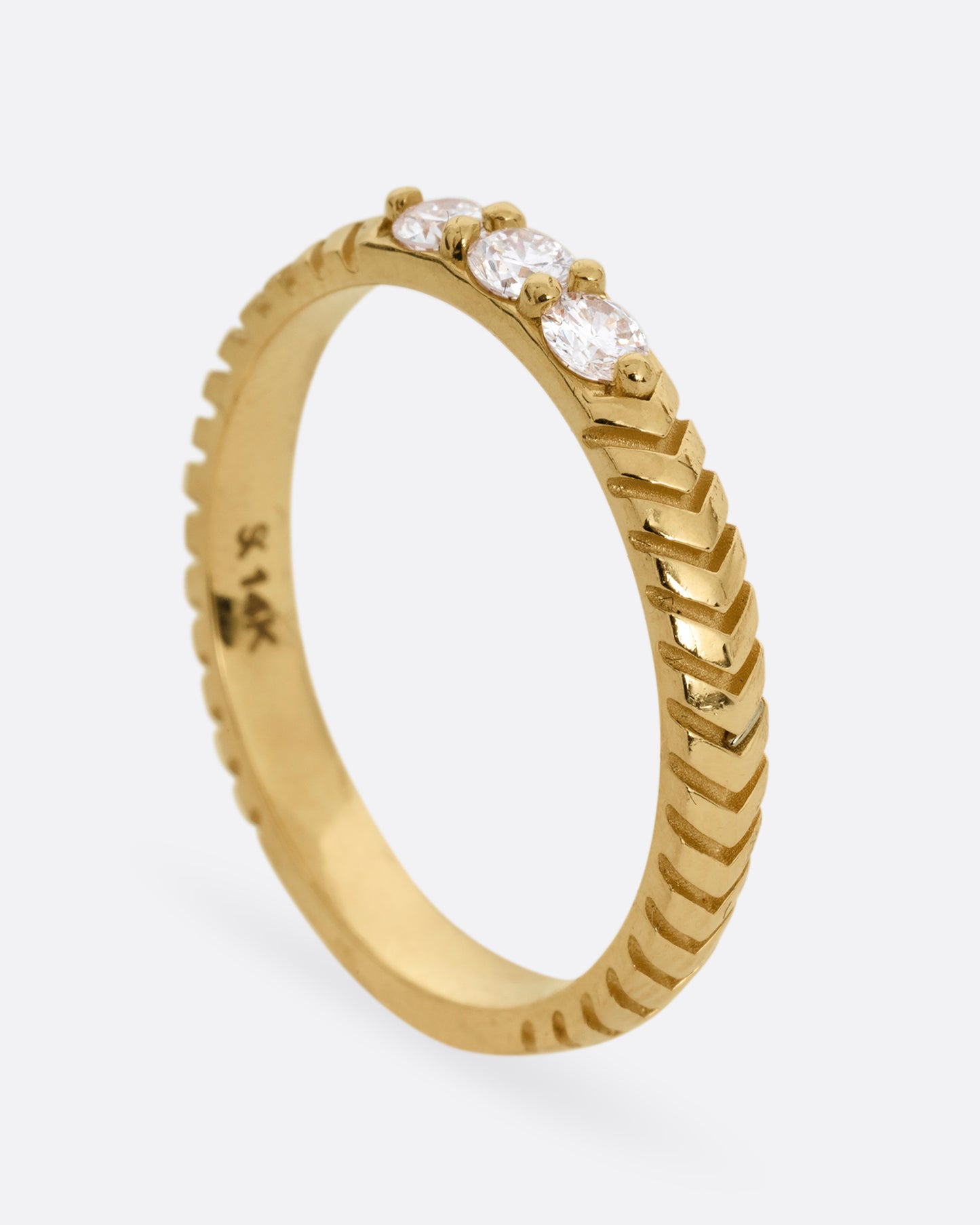 A yellow gold ring with arrow etching and three white diamonds. Shown from the side standing up.