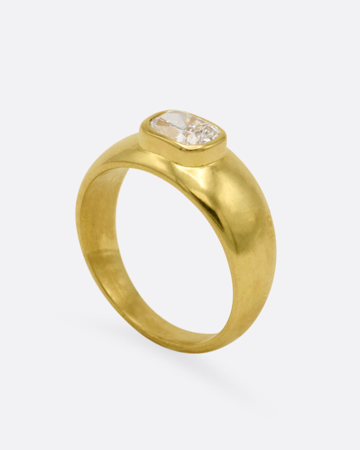 A yellow gold signet ring featuring a central cushion-cut diamond, shown from the side standing up.