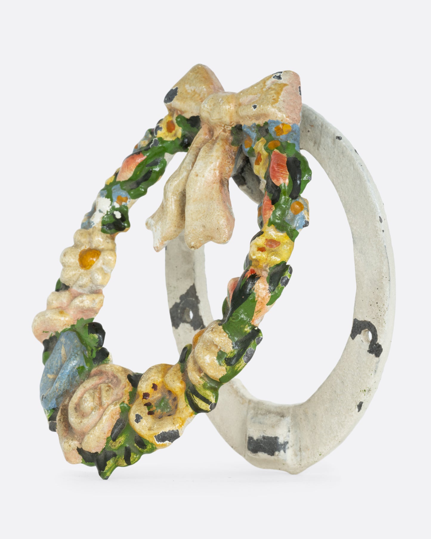 A cast iron wreath door knocker with a bow and flowers. Shown from the side.