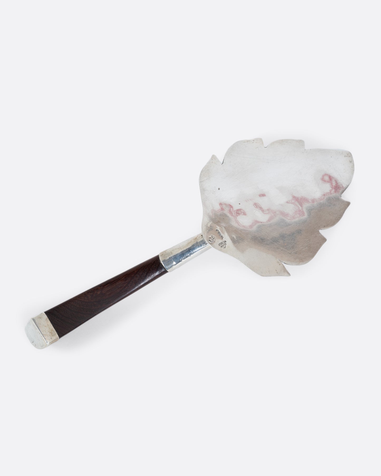 A silver leaf cake server with a wooden handle, shown from the back on its side.